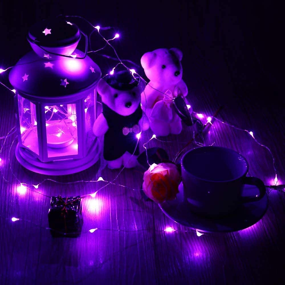 Nachtszene mit lila Lichtern. Teddybären, eine Laterne, eine Tasse, eine Rose und eine Geschenkbox auf Holzoberfläche.