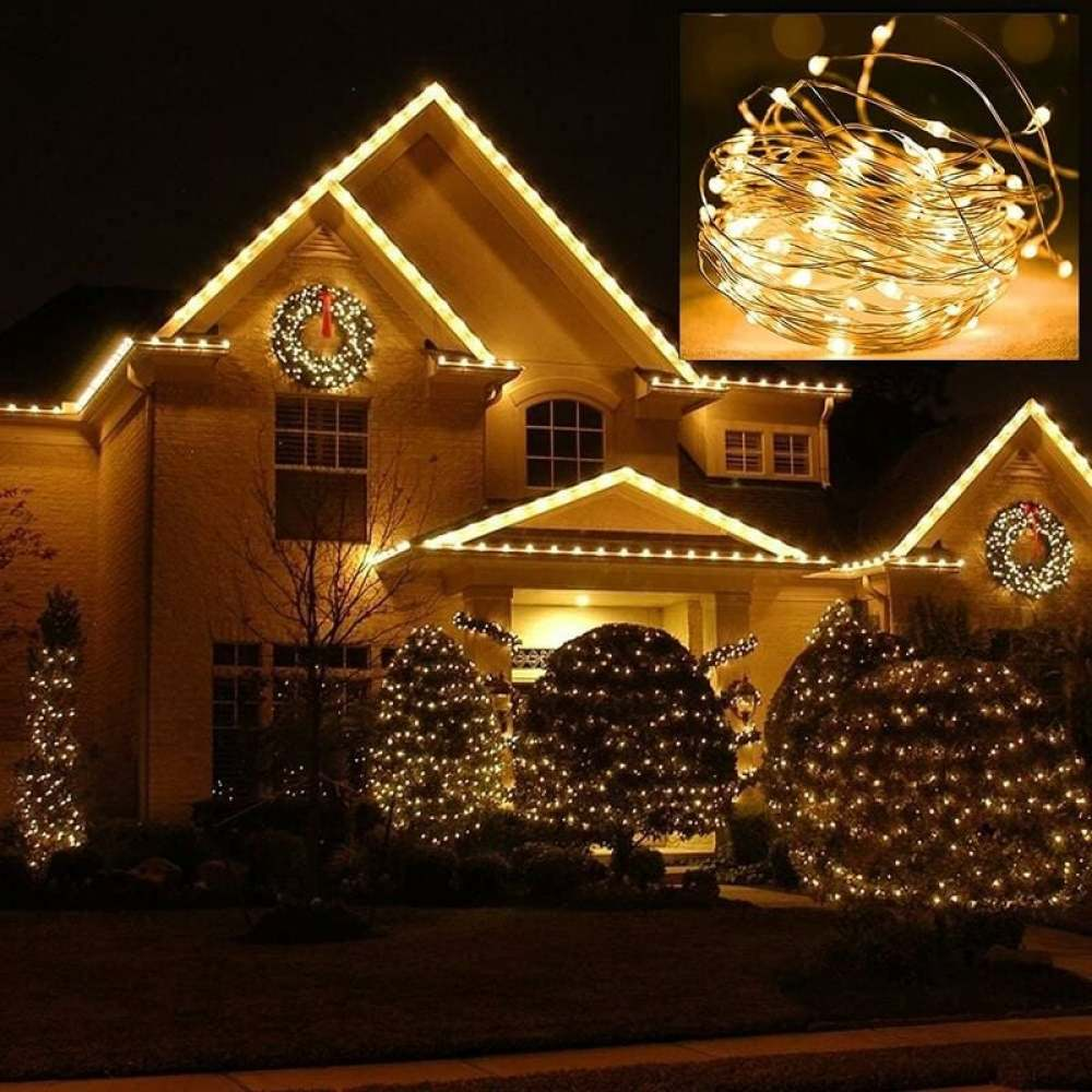 Ein mit Weihnachtslichtern geschmücktes Haus. Lichter befinden sich auf dem Dach, den Büschen und Bäumen. Kränze hängen vorne.