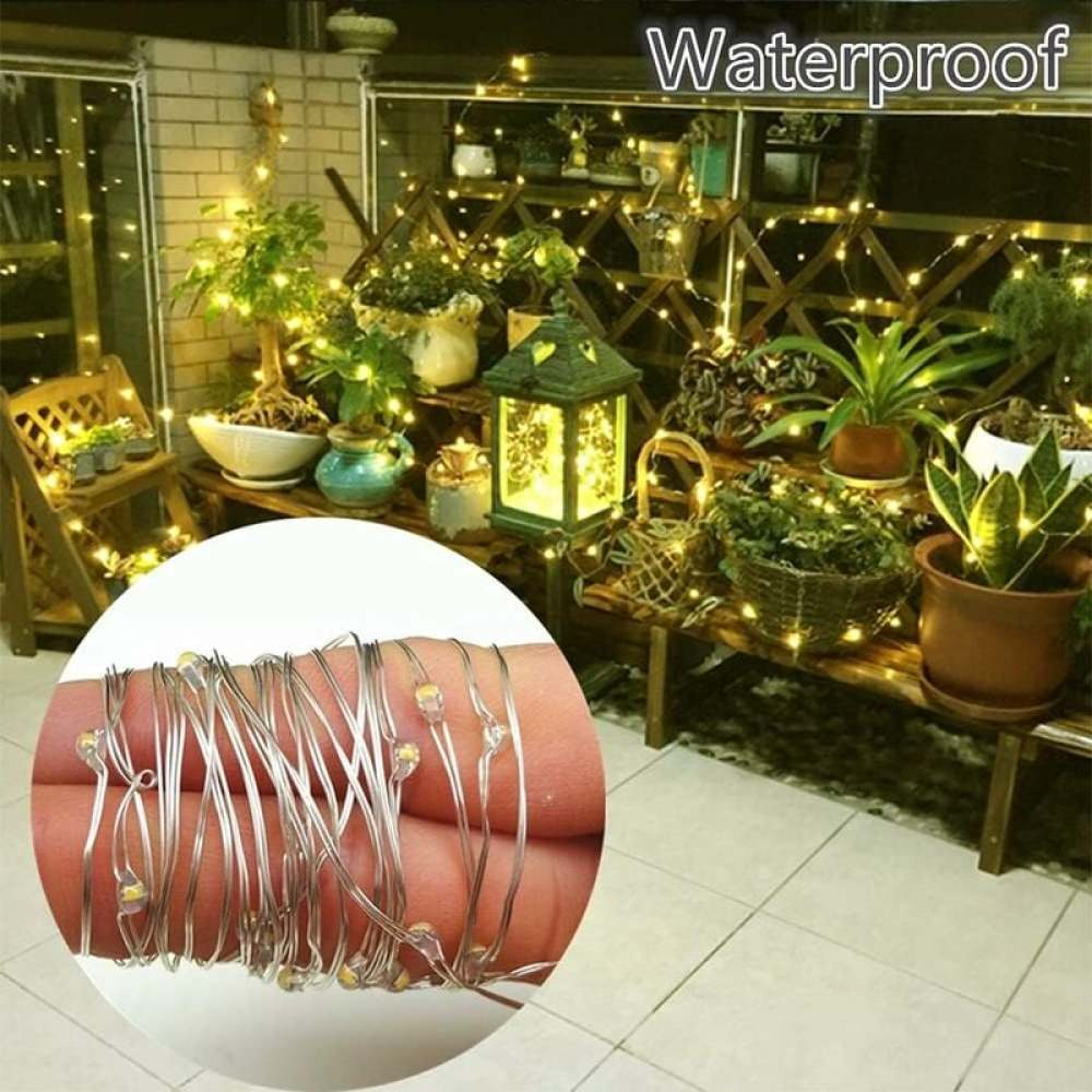 Nahaufnahme von LED-Lichterketten auf einem Finger. Hintergrund: Pflanzen, Laternen, Holzregale und das Wort 'Wasserdicht'.