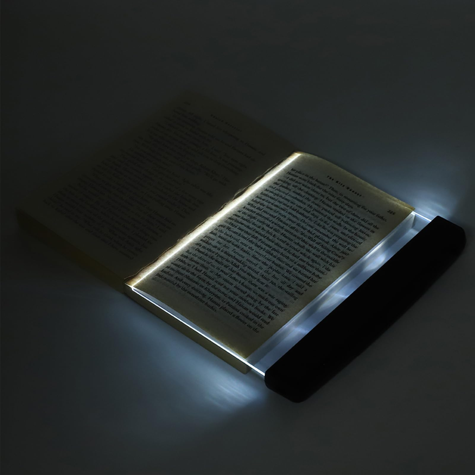 Ein offenes Buch mit einer Leselampe. Das Licht beleuchtet die Seiten mit Text. Ein dunkler Hintergrund.
