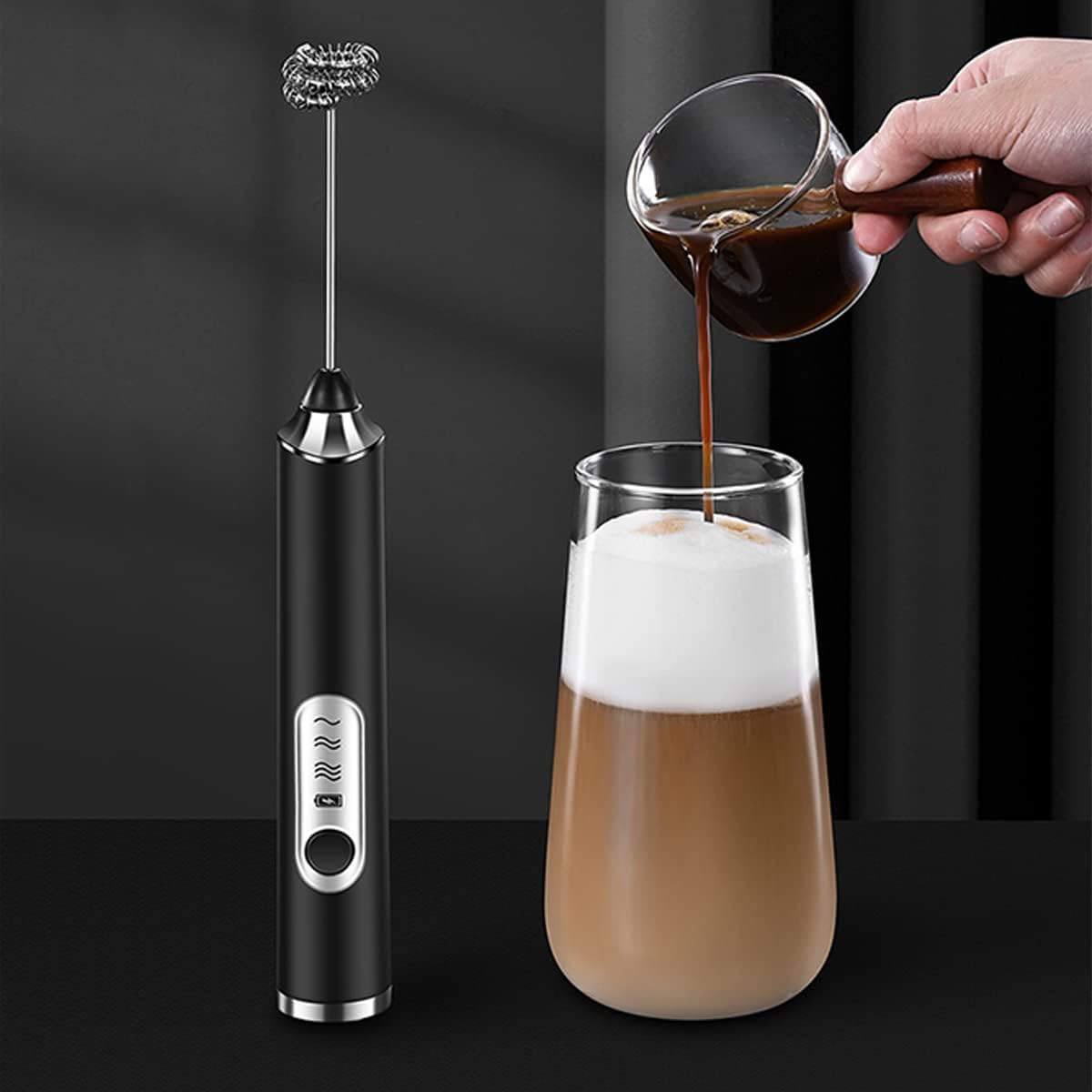 Ein Milchaufschäumer und ein Glas Kaffee mit Milch. Kaffee wird in das Glas gegossen. Der Hintergrund ist schwarz.