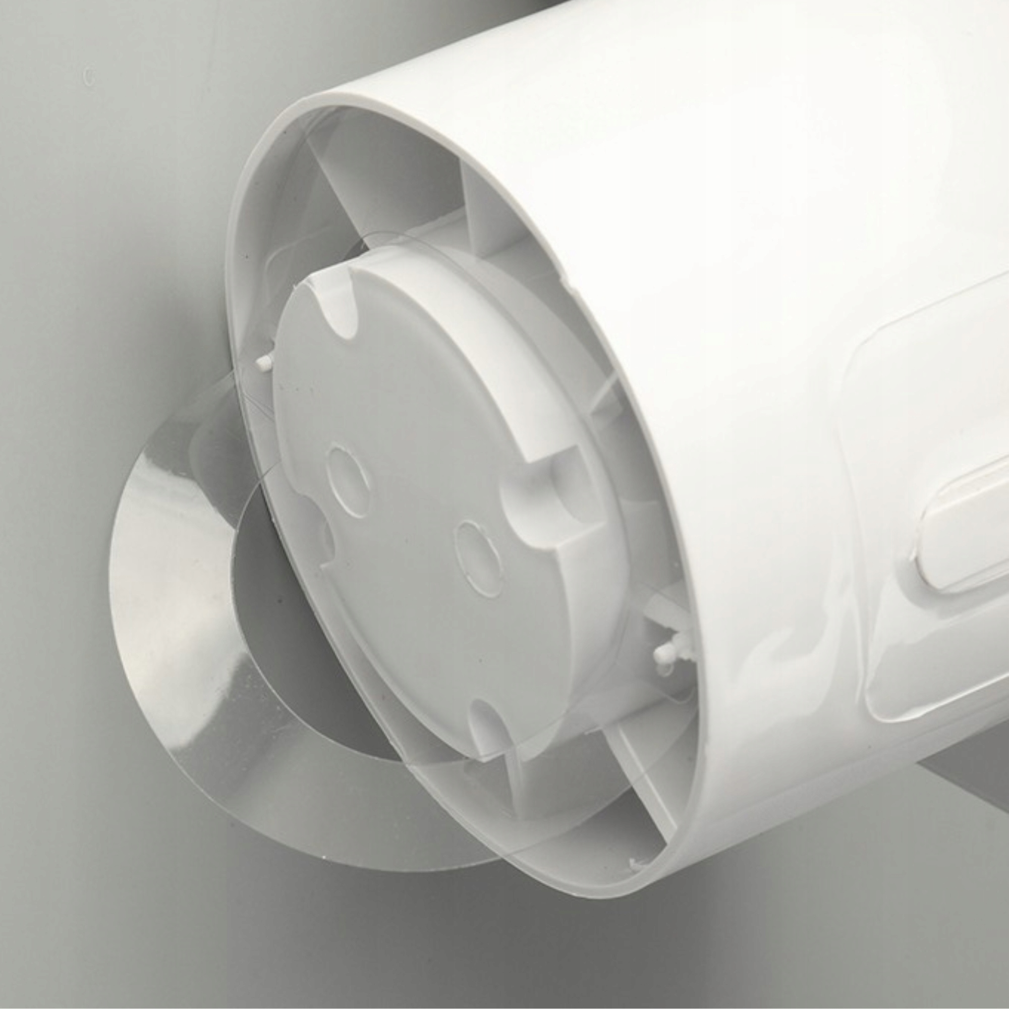 Zbliżenie białego plastikowego przedmiotu przymocowanego do szarej ściany. Obiekt ma okrągły kształt i przezroczyste plastikowe części.