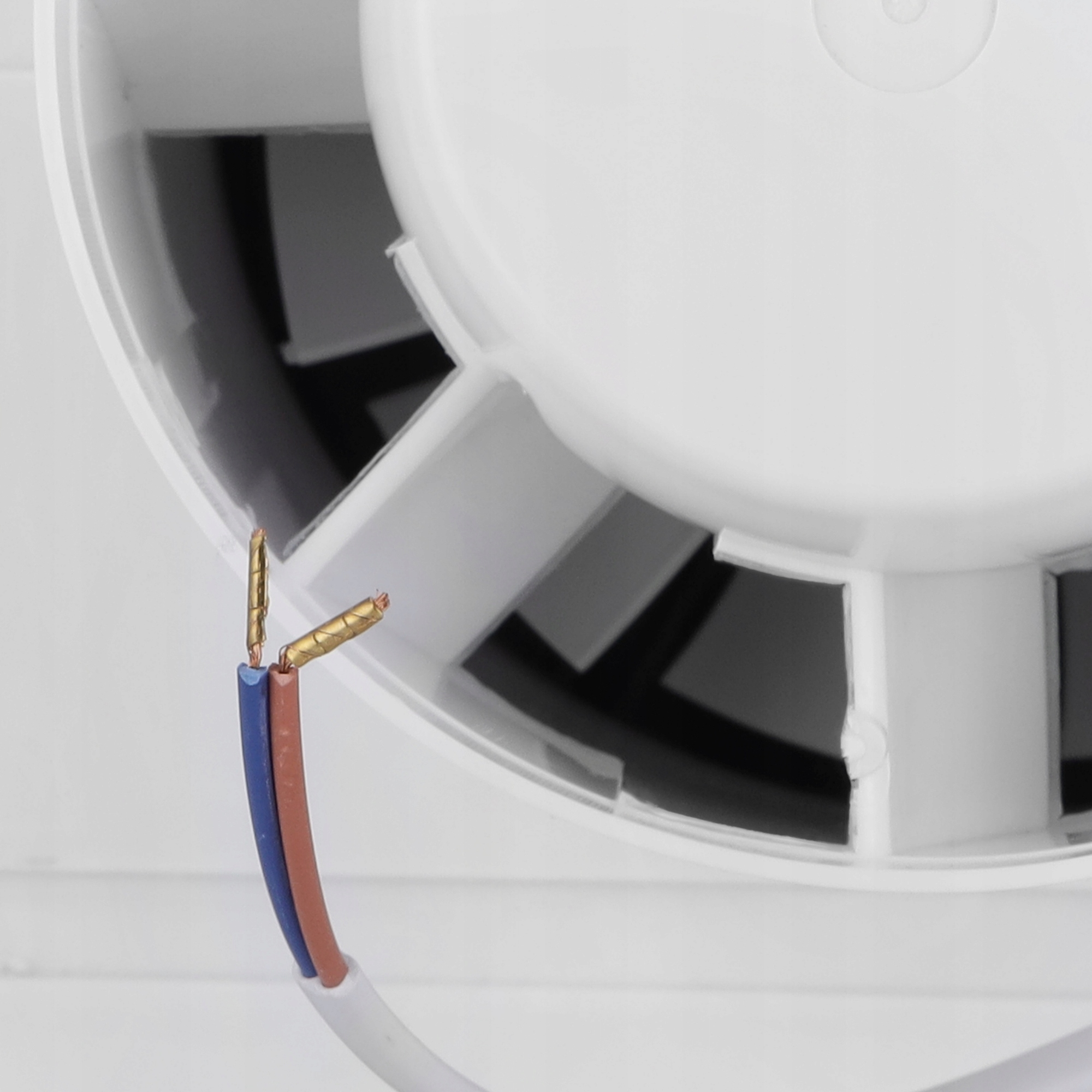 Zbliżenie białego wentylatora z odsłoniętymi przewodami. Niebieskie i brązowe przewody ze złotymi końcówkami wychodzą z wentylatora.