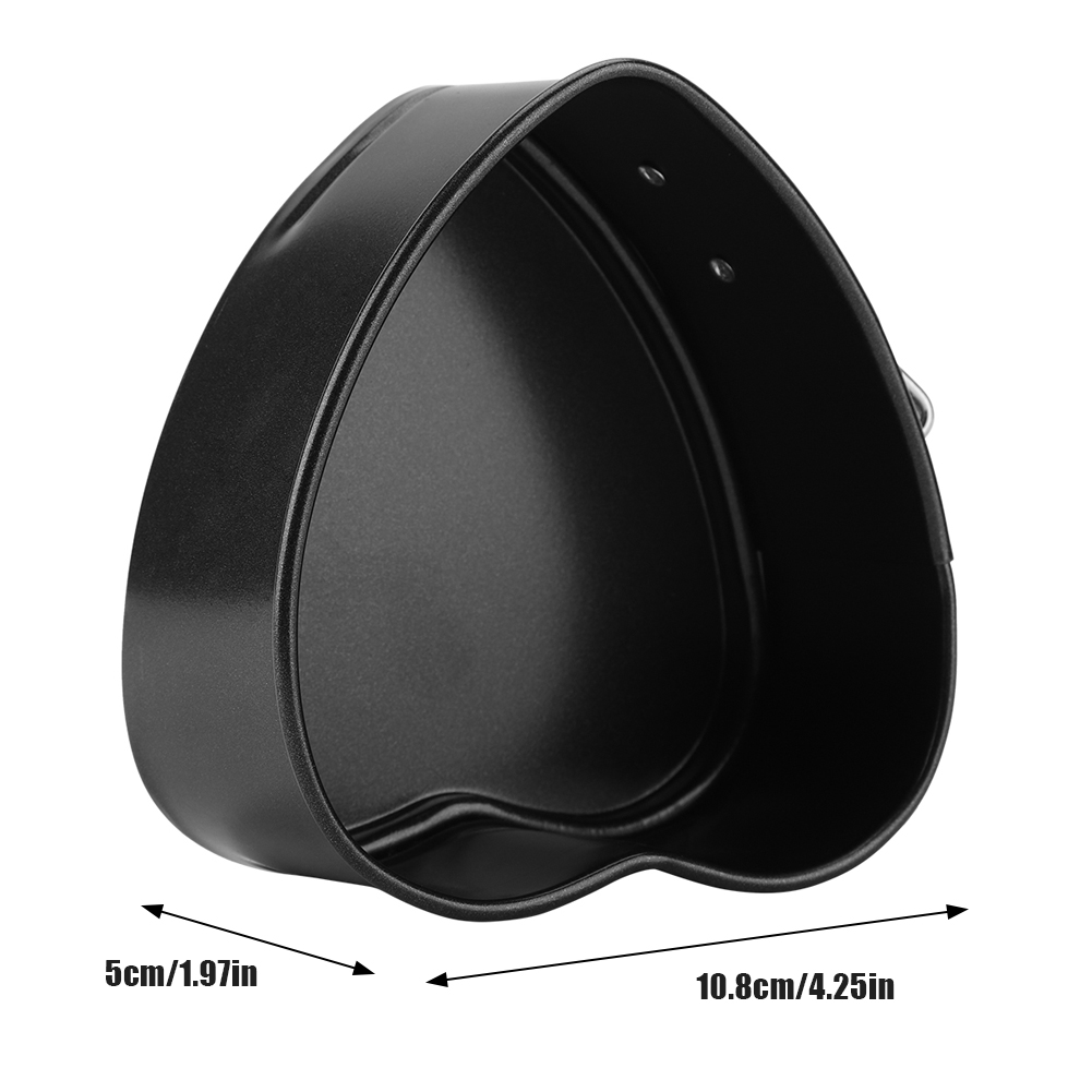 Eine schwarze herzförmige Backform. Maße: 5cm/1,97in und 10,8cm/4,25in. Sie ist leer und auf einer weißen Oberfläche.