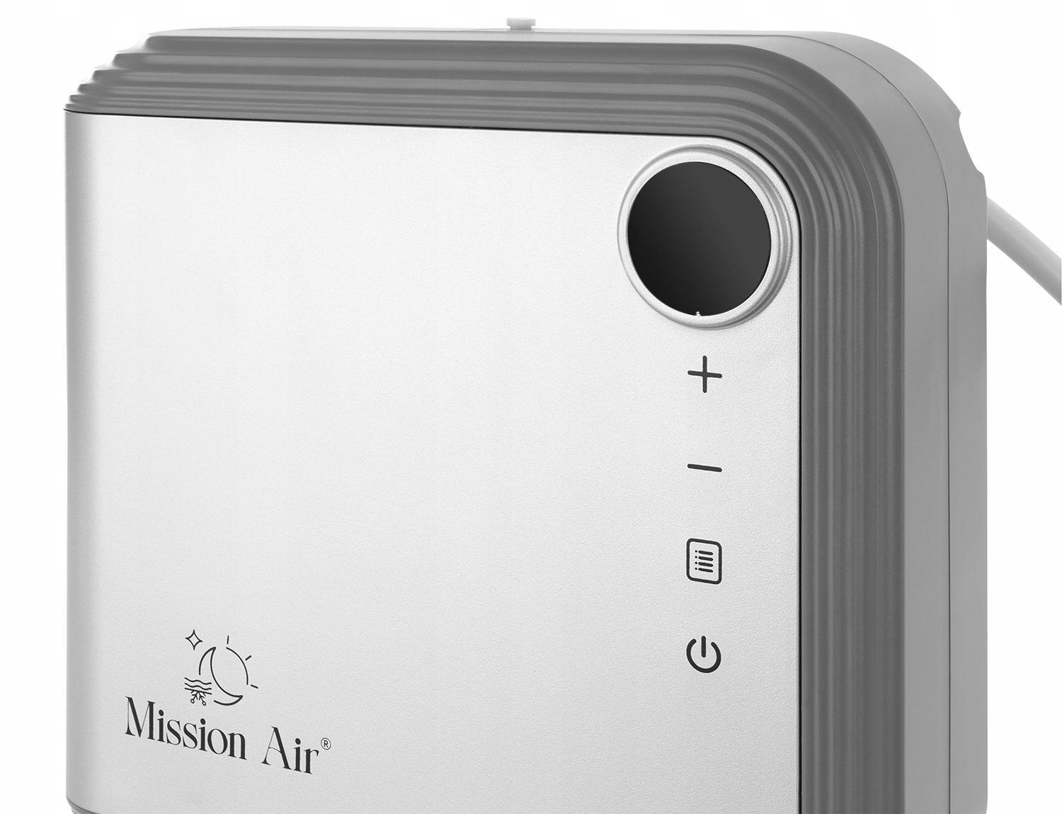 Zbliżenie urządzenia Mission Air. Ma srebrny przód, szare krawędzie i czarne koło ze znakami plus i minus. Widoczne są symbole zasilania i inne.