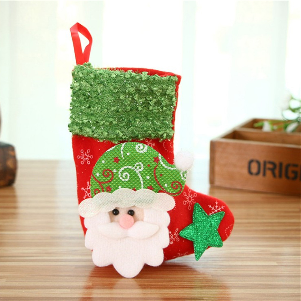 Ein Weihnachtsstrumpf. Rot mit grünem Oberteil und Santa-Gesicht. Er hat einen grünen Stern. Er sitzt auf einer Holzoberfläche.