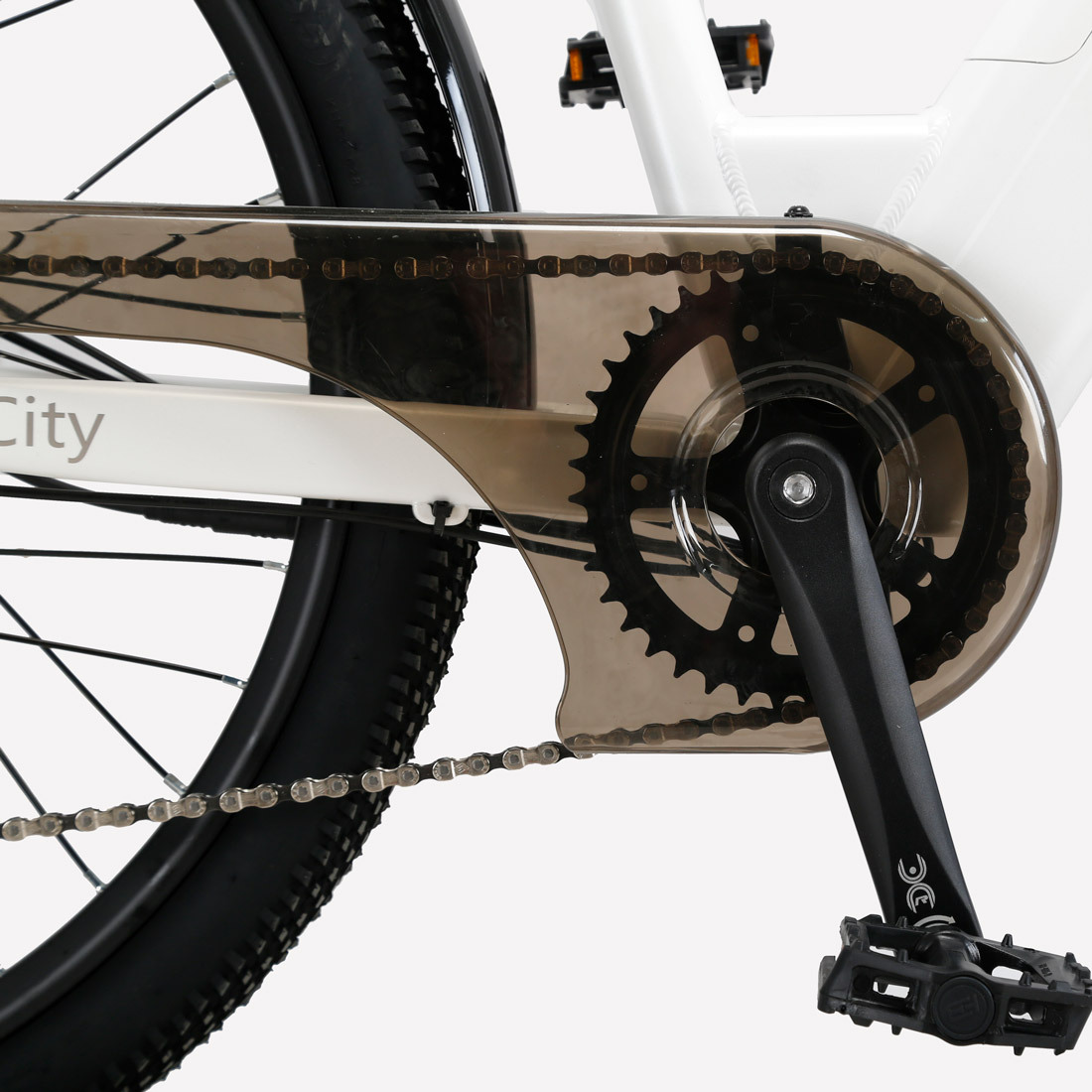 Zbliżenie napędu roweru. Pokazuje łańcuch, tarczę łańcuchową, pedał i koło. Rower ma białą ramę i czarną oponę.