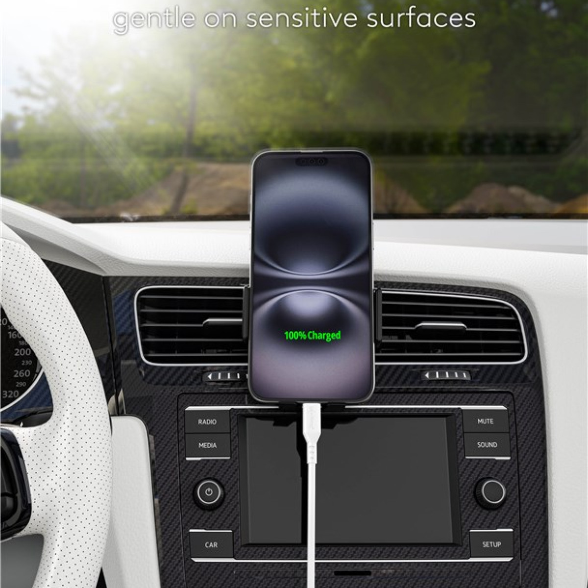Ein Telefon, das im Auto geladen wird. Das Telefon zeigt 100% geladen an. Der Hintergrund zeigt ein Armaturenbrett und verschwommene Bäume.