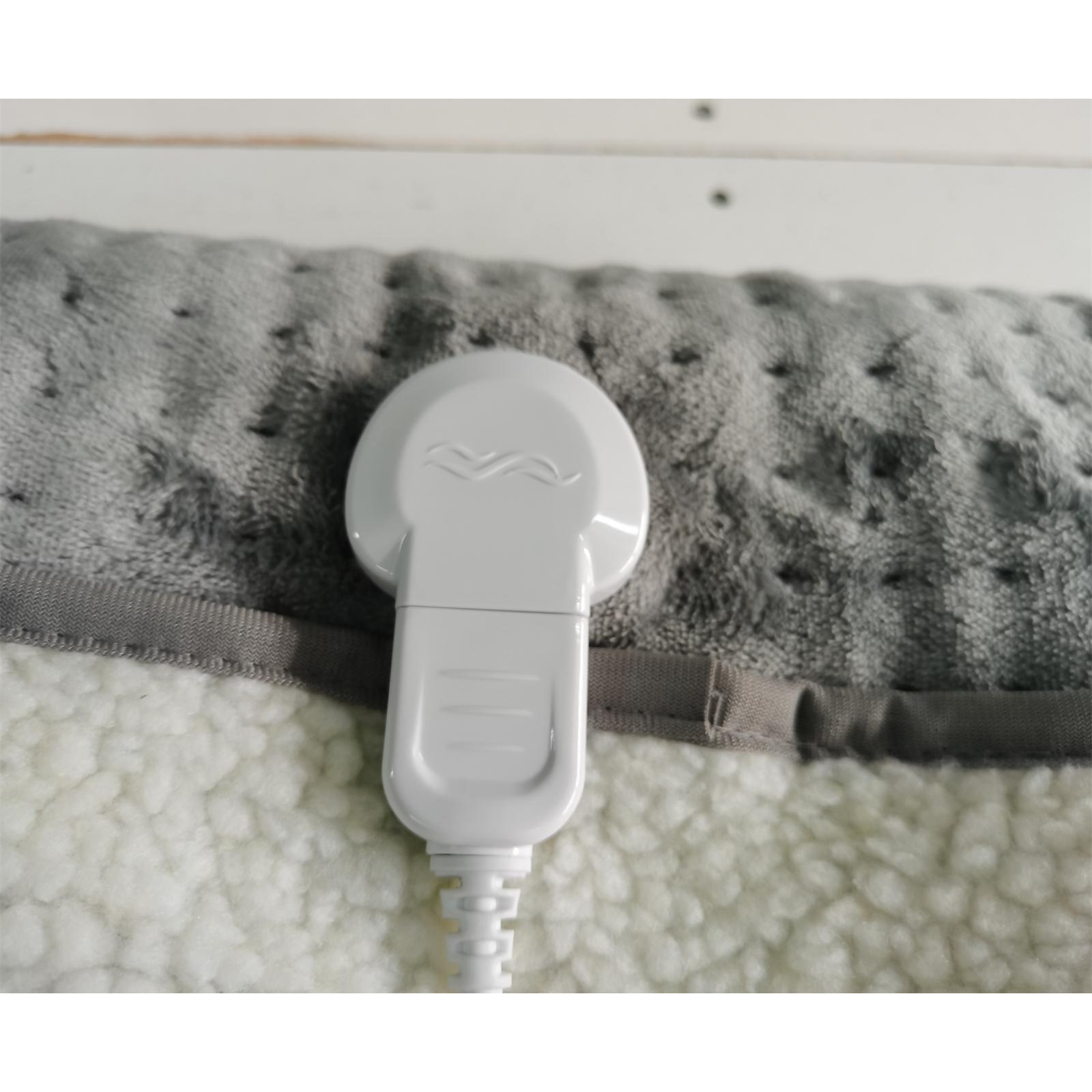 Ein weißer Heizkissen-Controller befindet sich auf einem grau-weißen Heizkissen. Der Hintergrund ist eine weiße Holzoberfläche.