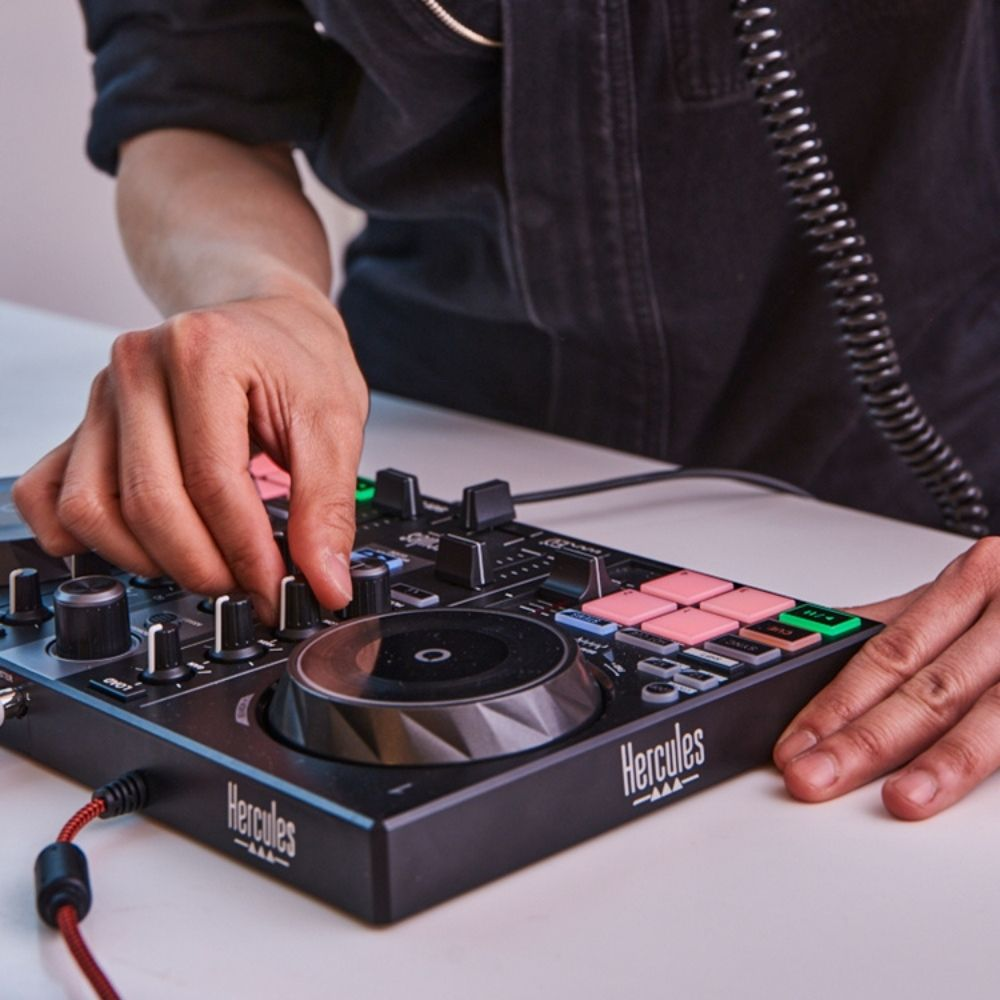 A person's hands adjusting a black DJ controller with pink and green buttons on a white surface.
