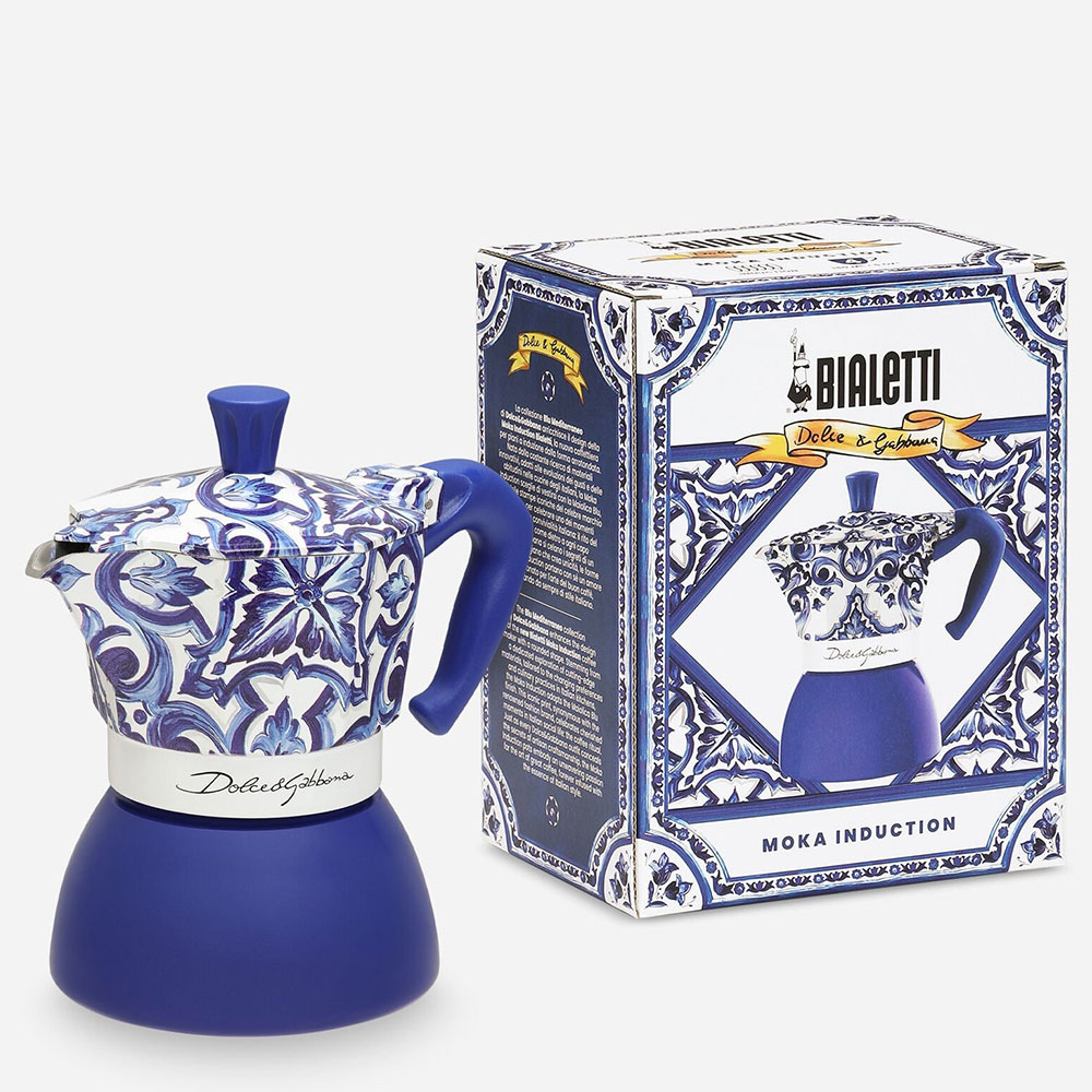 Una caffettiera Bialetti Dolce & Gabbana blu e bianca accanto alla sua scatola, entrambe con motivi floreali.