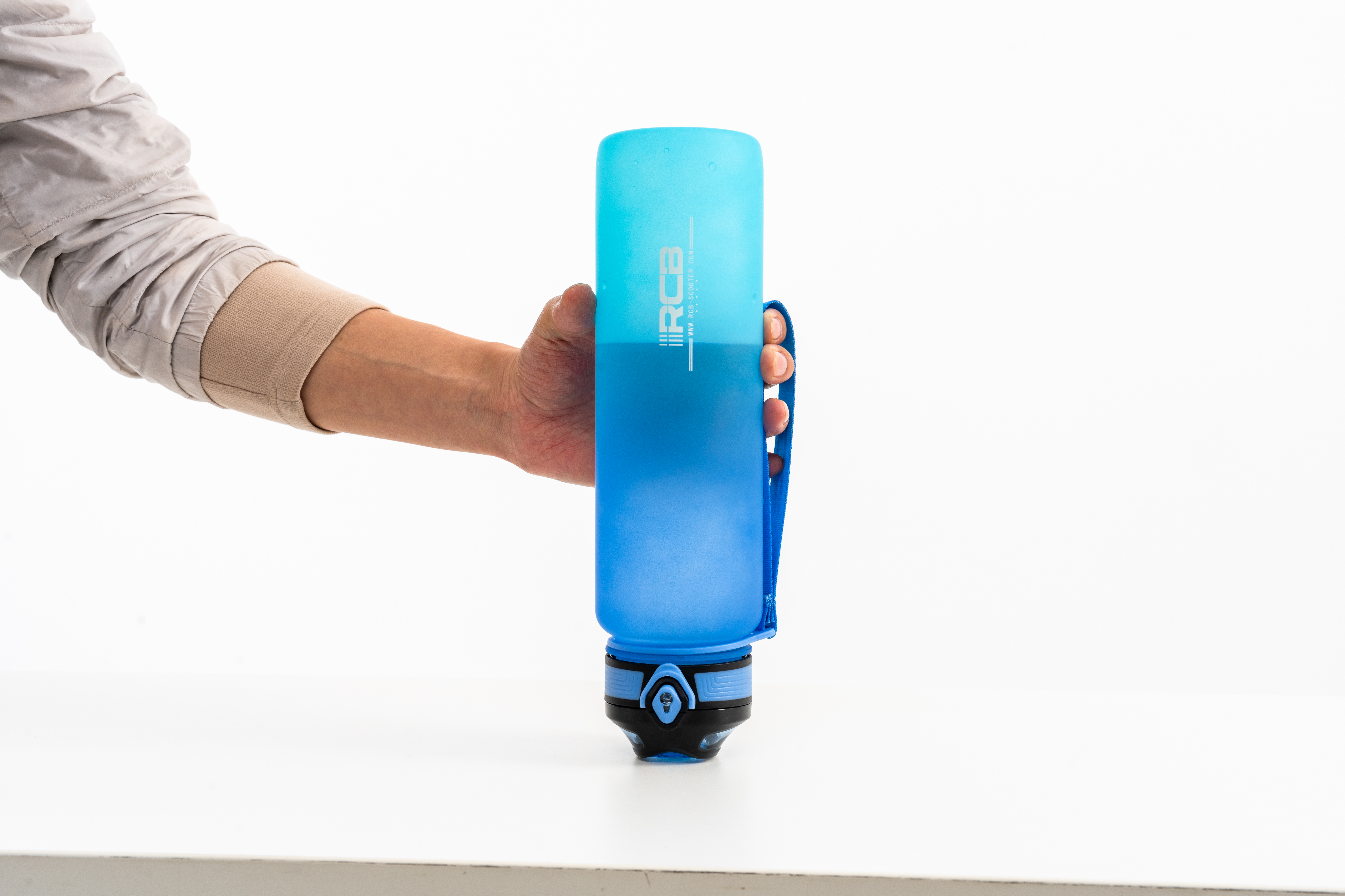 Een hand houdt een blauwe waterfles met een blauwe riem vast. De achtergrond is wit.