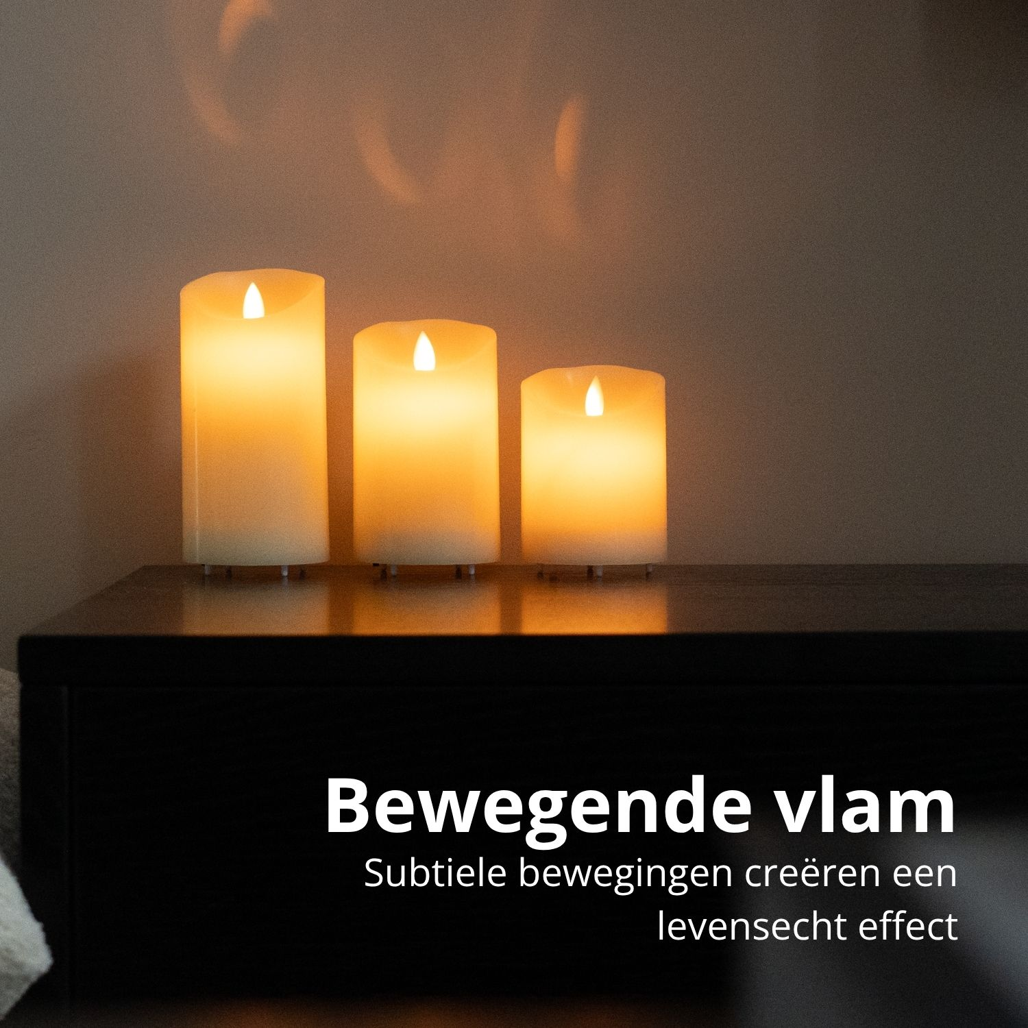 Drie brandende, ivoorkleurige kaarsen van verschillende hoogtes staan op een zwart oppervlak. Tekst daaronder luidt 'Bewegende vlam'.