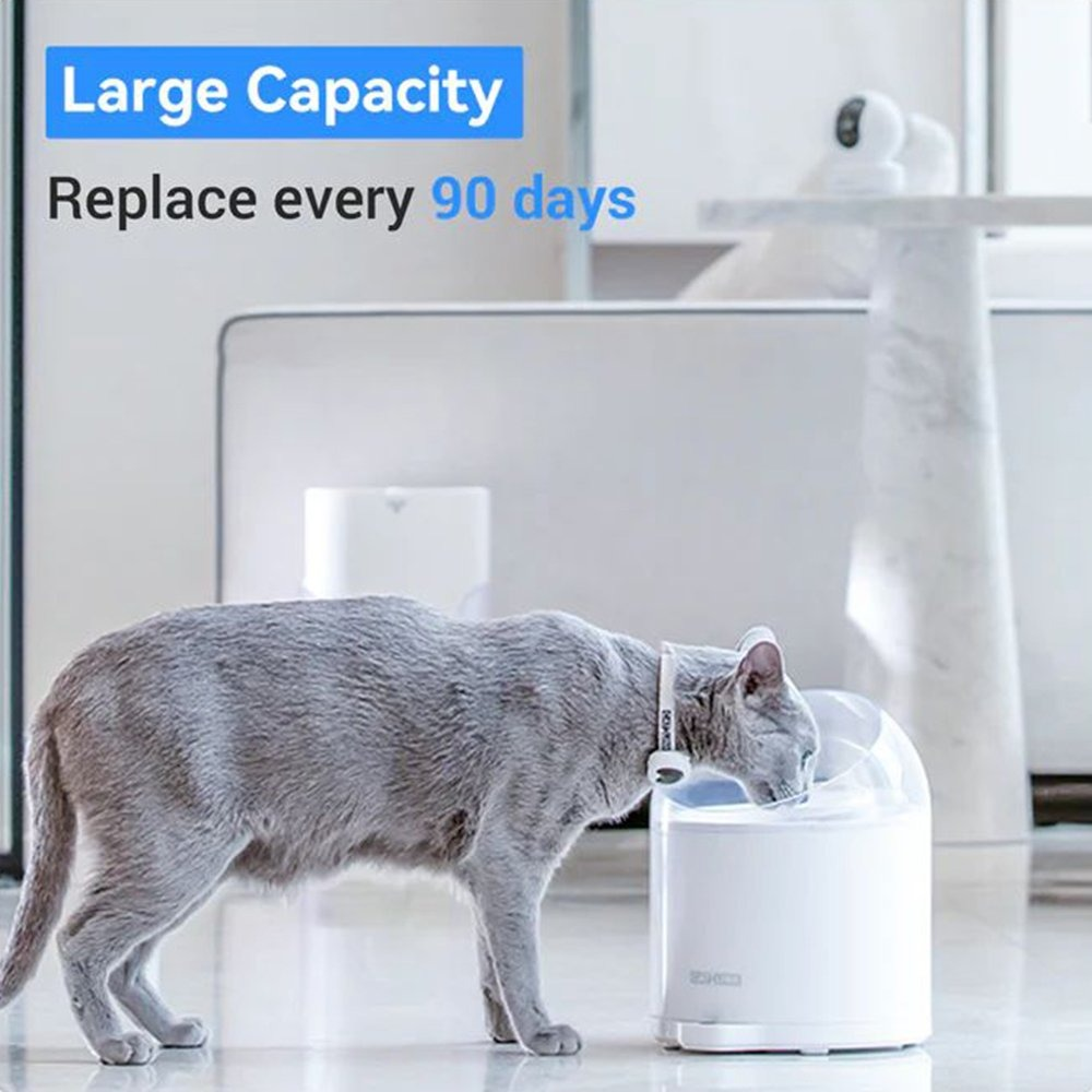 A gray cat drinks from a white water fountain. The text reads 'Large Capacity' and 'Replace every 90 days'. Background is blurred.