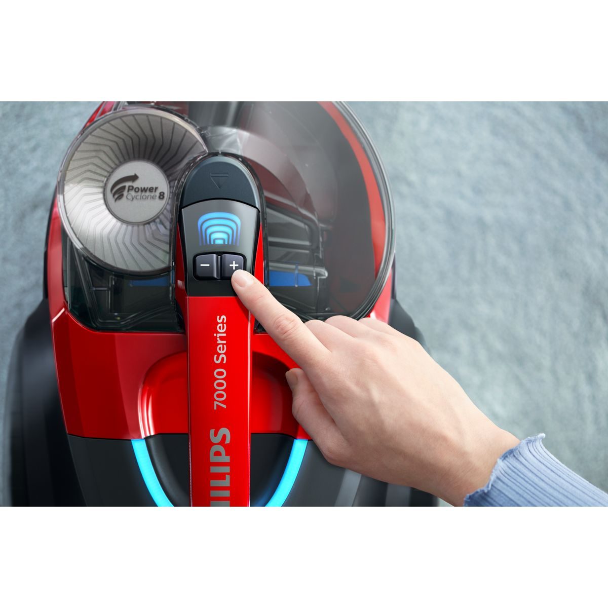 Dłoń naciska przycisk plus na czerwonym odkurzaczu Philips. Odkurzacz posiada funkcję Power Cyclone 8.