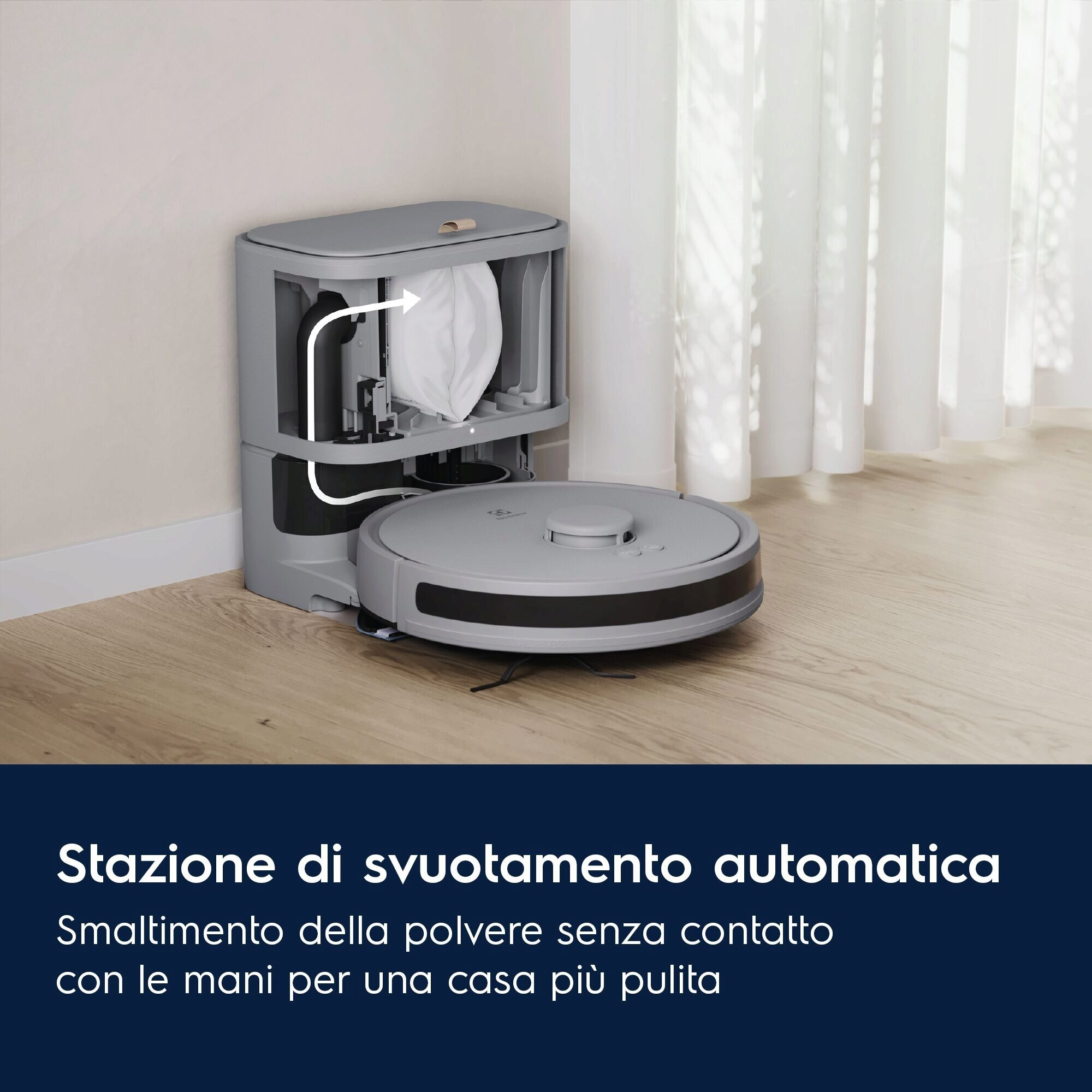 Un aspirapolvere robot grigio e una stazione di svuotamento automatico su un pavimento in legno, vicino a una tenda bianca.