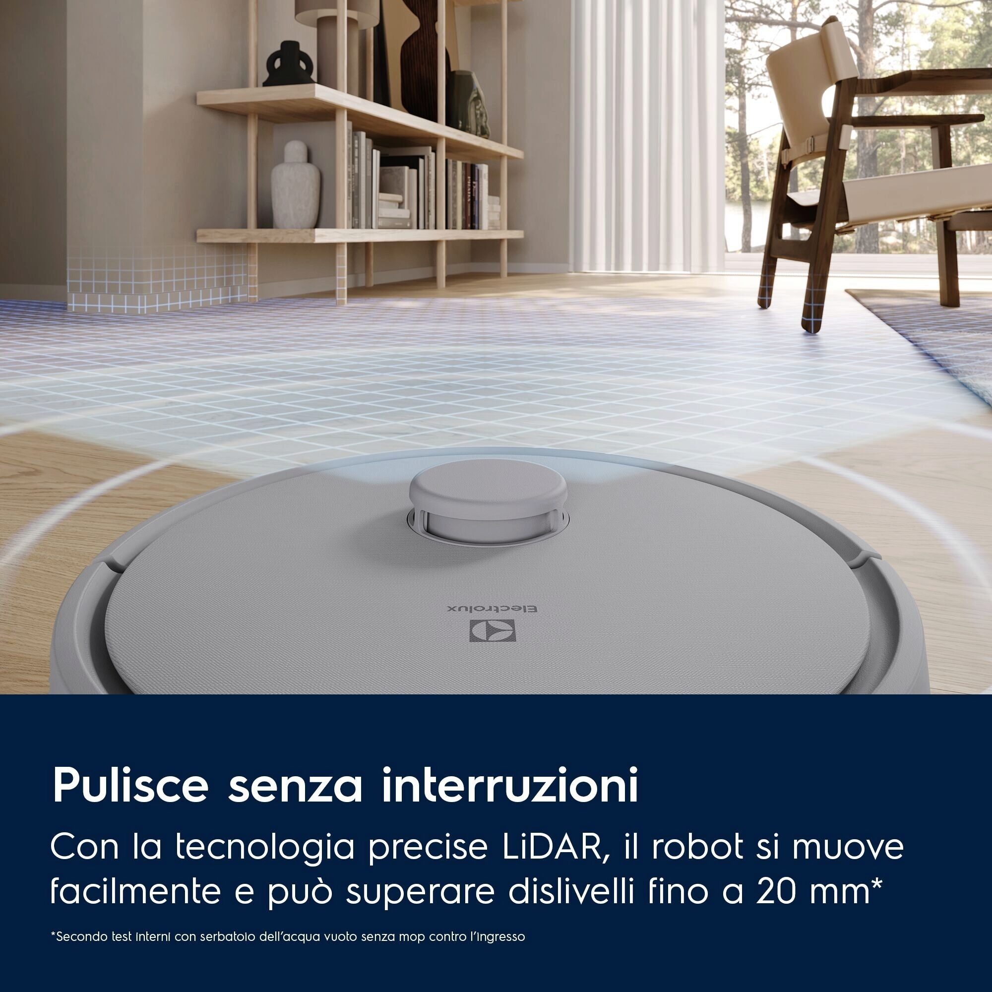 Un aspirapolvere robot grigio su un pavimento in legno. Una sedia e mensole sono visibili sullo sfondo.