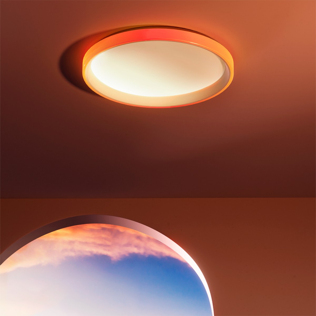 Nowoczesna pomarańczowa lampa sufitowa oświetla górę, z przebłyskiem nieba przez łuk poniżej. Kolory: pomarańczowy, niebieski, biały.