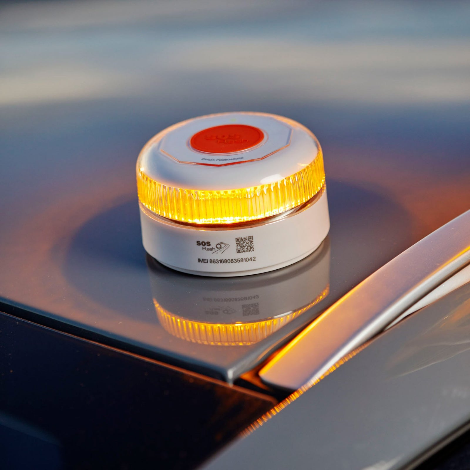 Un dispositivo de flash SOS blanco y naranja en un coche. El dispositivo brilla en amarillo. El fondo es un cielo borroso.