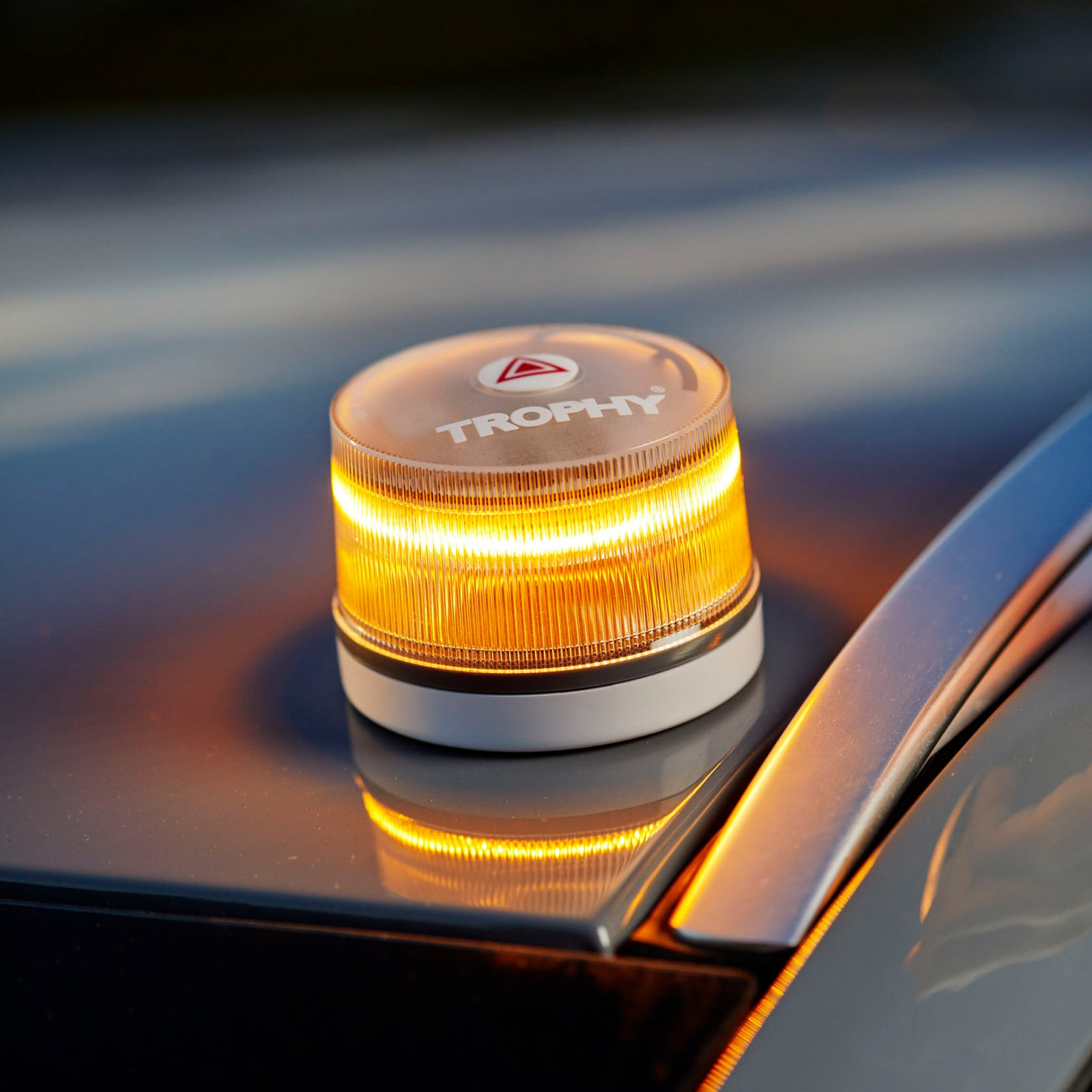 Una luz giratoria ámbar con la etiqueta 'TROPHY' está sobre un coche. La luz tiene una base blanca y una cubierta transparente.