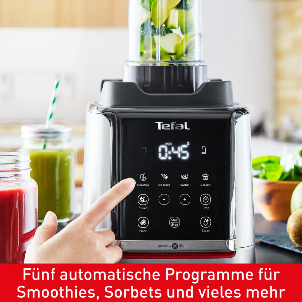 Ein Tefal-Mixer mit einer Hand, die die Smoothie-Taste drückt. Der Mixer hat einen Timer und ist mit grünen Früchten gefüllt.