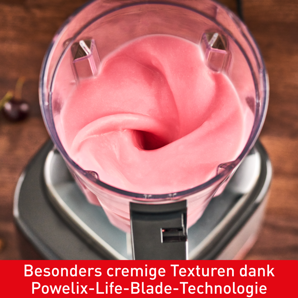 Ein Mixer ist mit rosa Flüssigkeit gefüllt, möglicherweise ein Smoothie, in Bewegung. Der Hintergrund hat eine Holzoberfläche und eine Kirsche.