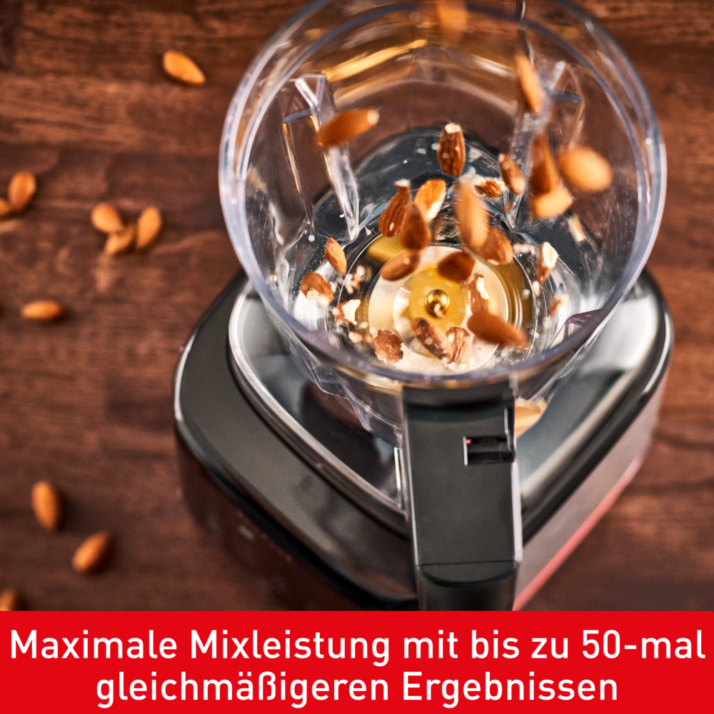 Ein Mixer mit Mandeln, die hineinfallen. Der Mixer steht auf einer Holzoberfläche. Text unten: Maximale Mixleistung.