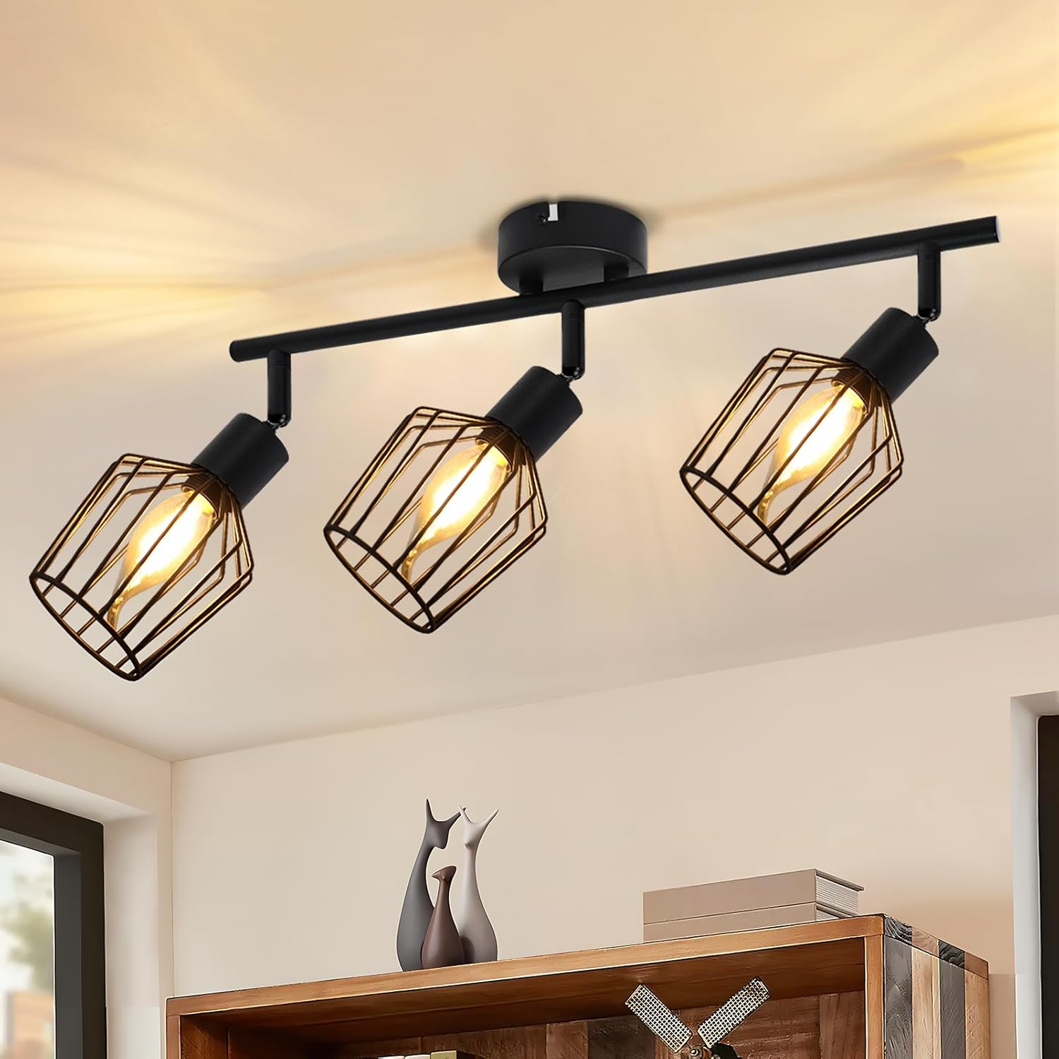 Tre lampade a sospensione a gabbia nera su un soffitto. Sotto, una mensola con vasi decorativi e libri.