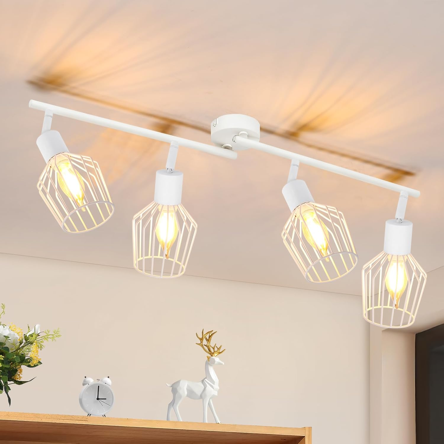 Faretti bianchi a soffitto con paralumi a gabbia. Sotto, una mensola con orologio, fiori e una statuina di cervo. La luce brilla sul soffitto.