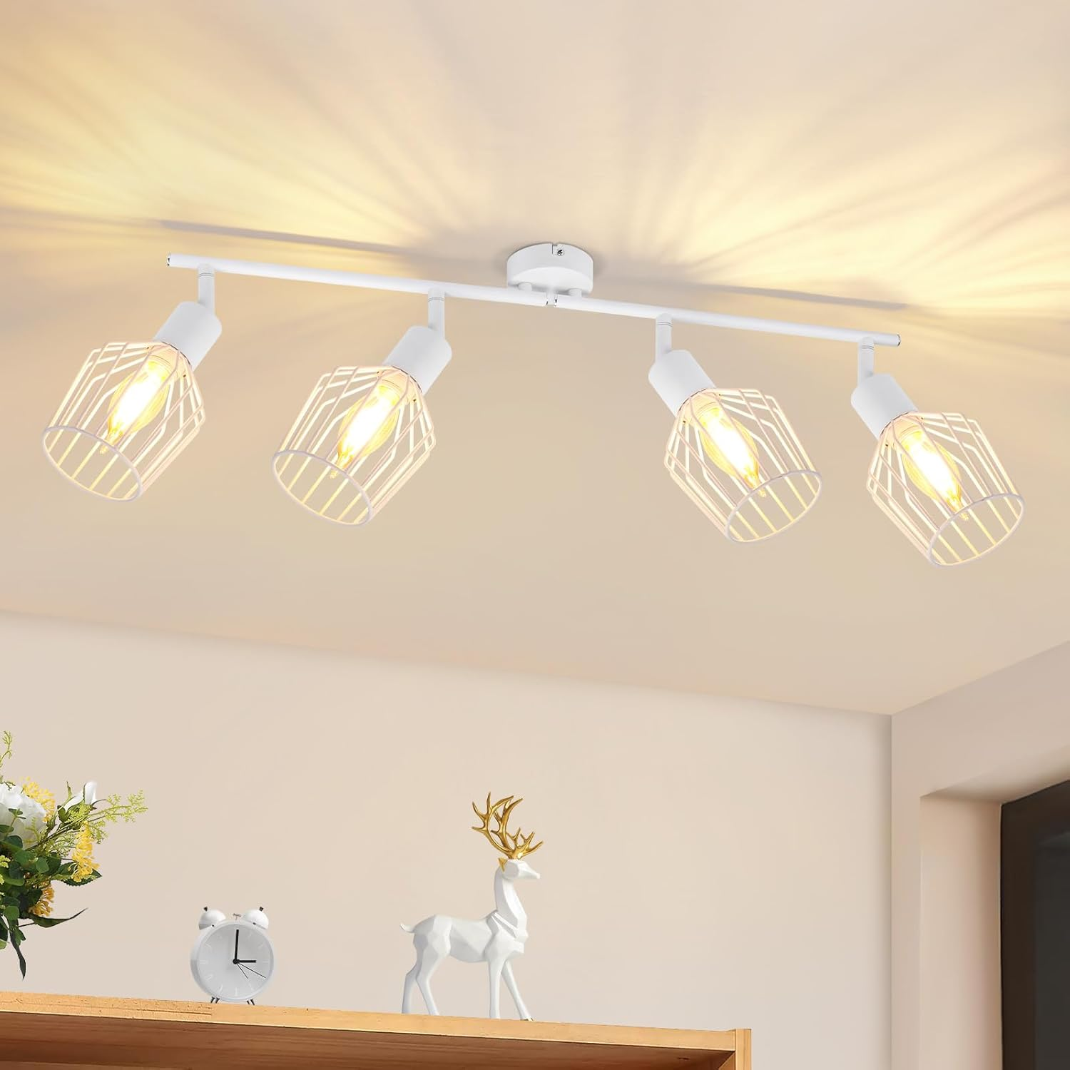 Eine weiße Deckenleuchte mit vier käfigartigen Lampen. Darunter ein Regal mit Uhr, Blumen und einer Hirschstatue.