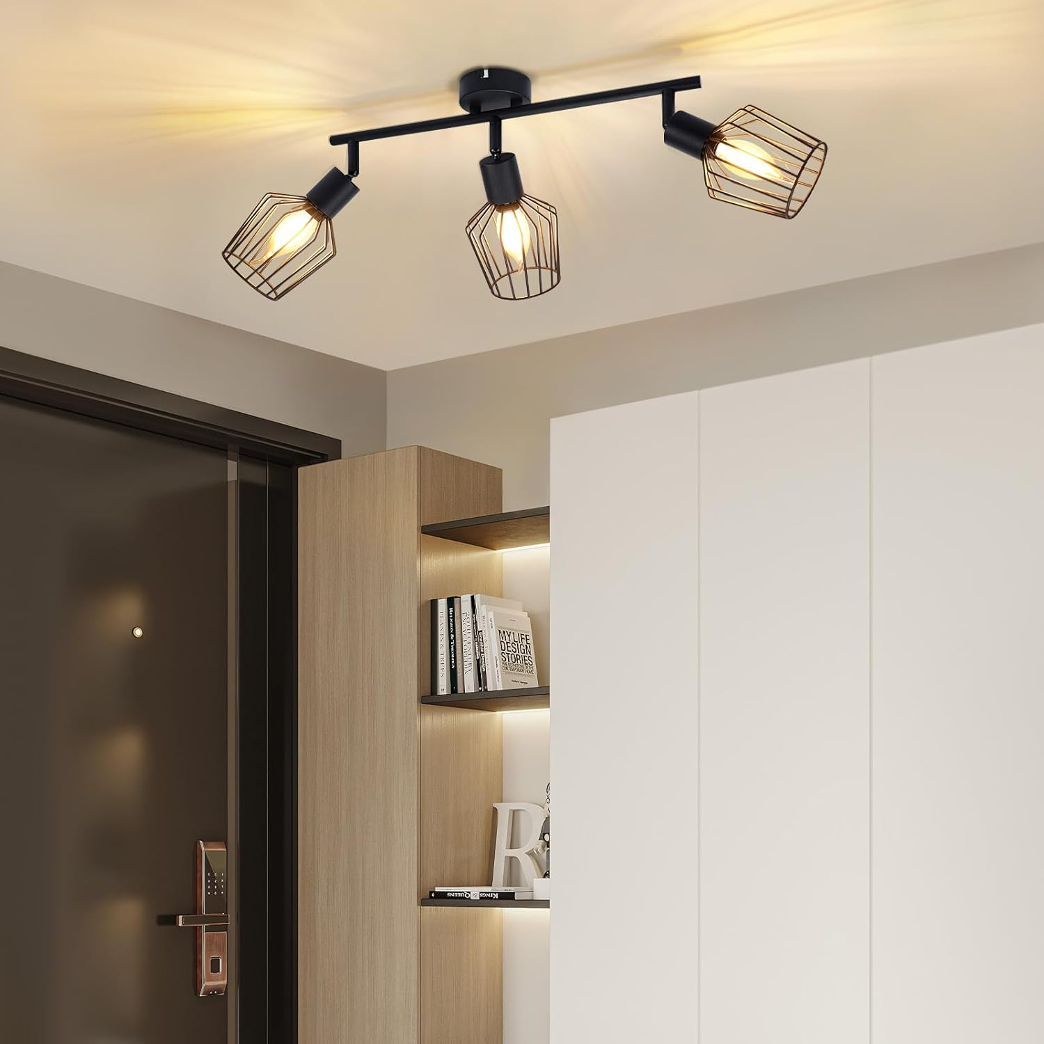 Eine moderne Deckenleuchte mit drei schwarzen käfigartigen Lampen. Die Szene umfasst eine Tür, Regale mit Büchern und einen weißen Schrank.