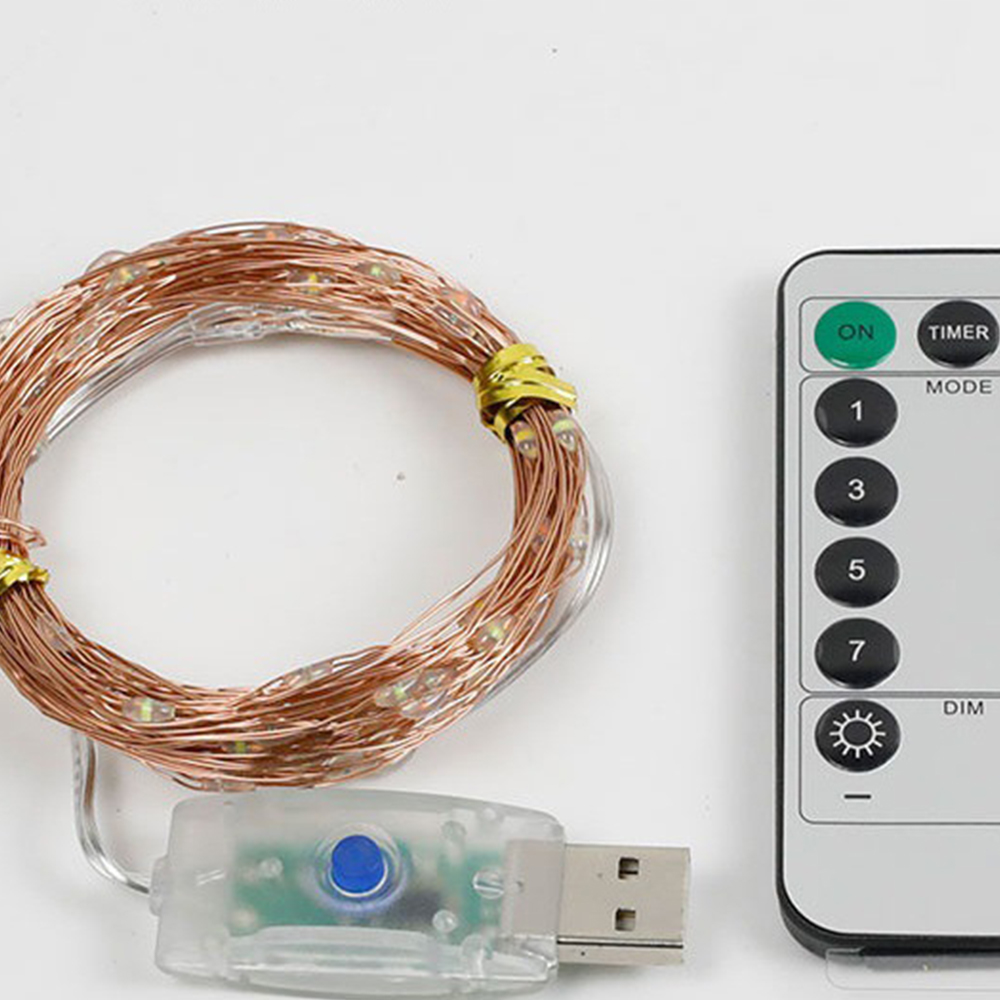 Ein Bündel Kupferdraht-LED-Leuchten, ein USB-Anschluss und eine Fernbedienung liegen auf einer weißen Oberfläche.