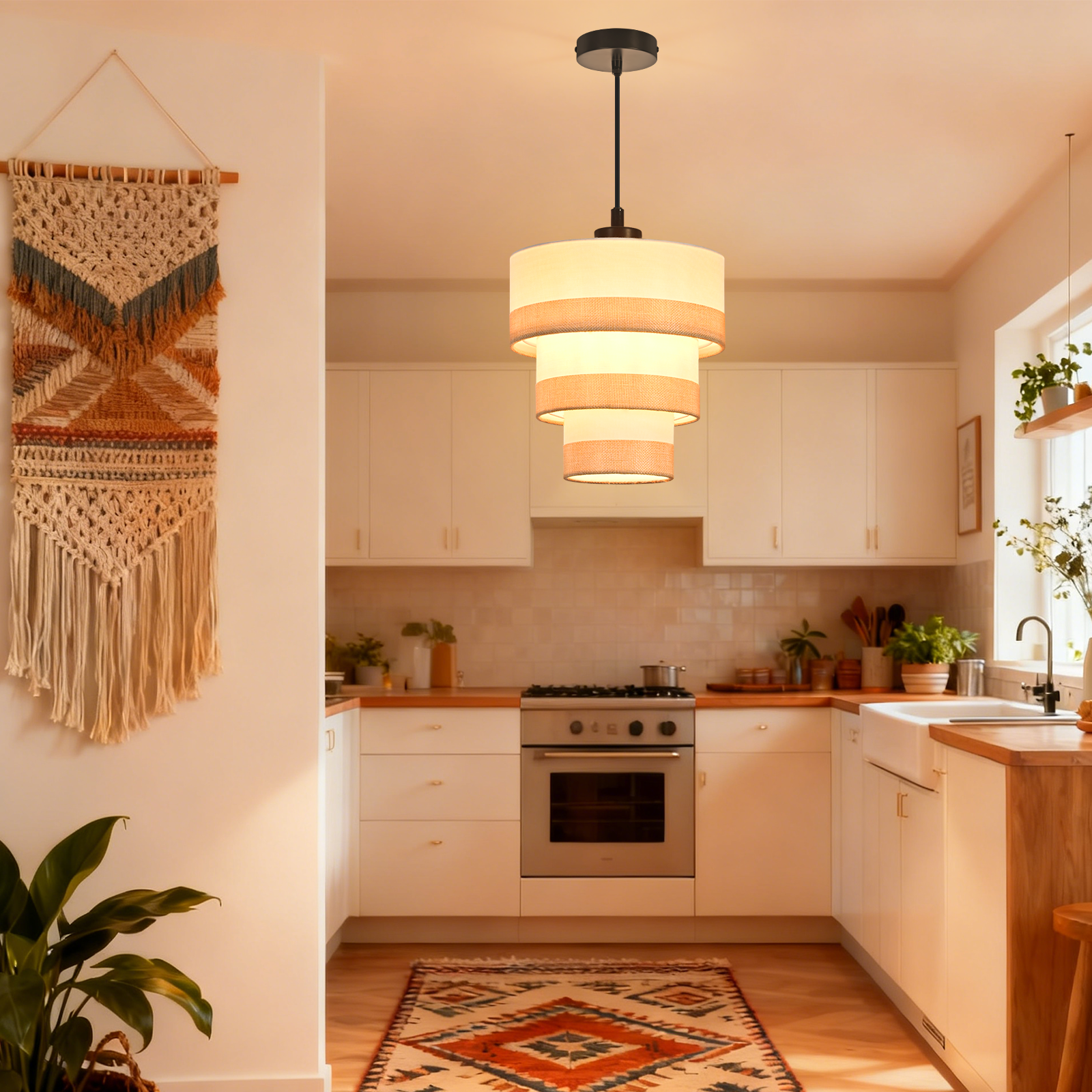 Kuchnia z lampą wiszącą, dywanem, kuchenką i makramą na ścianie. Białe szafki, drewniany blat i rośliny.