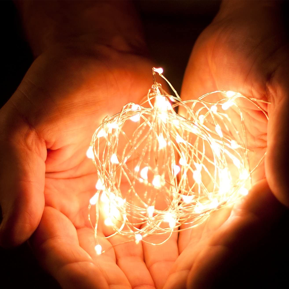 Hände, die eine Schnur mit leuchtenden Lichterketten umfassen. Die Lichter sind warmweiß und der Hintergrund ist dunkel.