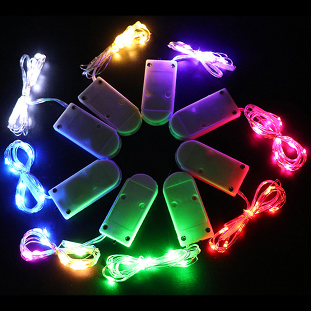 Neun Batteriepacks mit bunten LED-Lichterketten, die auf einer schwarzen Oberfläche kreisförmig angeordnet sind. Verschiedene Farben: weiß, blau, grün, rot, gelb.