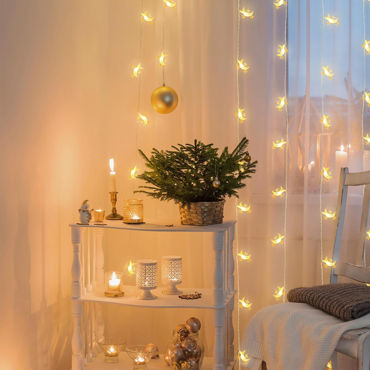 Festliche Szene mit kleinem Weihnachtsbaum, Lichtern, Kerzen und Dekorationen auf einem weißen Tisch. Ein Stuhl mit Decke rechts.