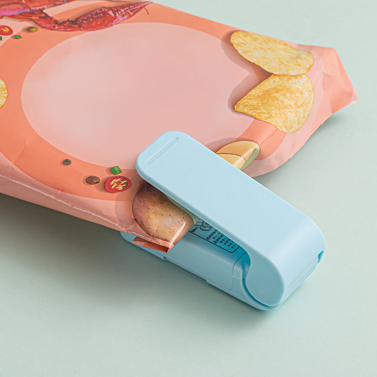 Ein blaues Beutelversiegelungsgerät verschließt eine Chipstüte. Chips sind auf dem Beutel sichtbar. Der Hintergrund ist eine hellgrüne Oberfläche.