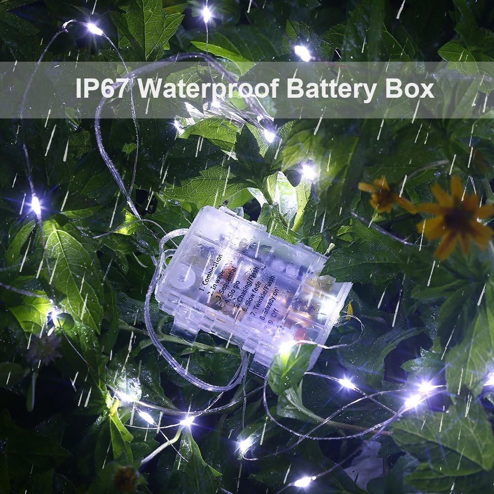 Lichterketten mit Batteriebox in grünem Laub. Die Box hat mehrere Lichtmodi. Die Szene deutet auf eine regnerische Umgebung im Freien hin.