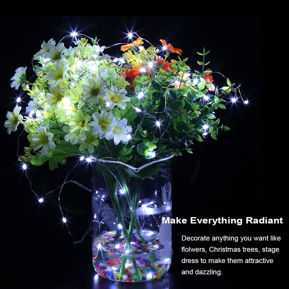 Eine Vase mit Blumen und Lichtern. Die Blumen haben weiße und gelbe Blütenblätter und orangefarbene. Die Lichter sind klein und hell.