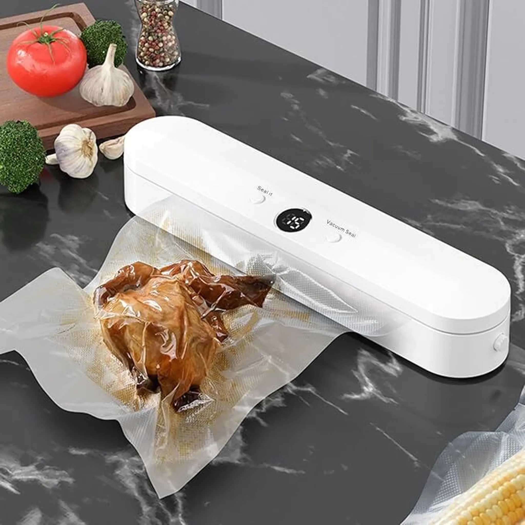 Ein weißer Vakuumierer mit einem verpackten Hähnchen. Außerdem eine Tomate, Knoblauch, Brokkoli und ein Pfeffermörser.