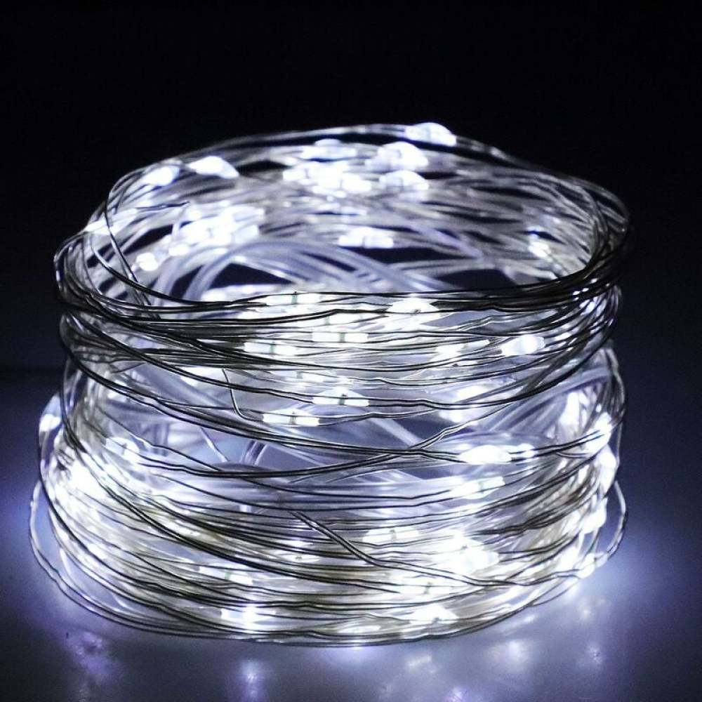 Eine Spule aus silbernen Drahtlichtern, beleuchtet mit hellen weißen Lichtern, liegt auf einer reflektierenden Oberfläche vor dunklem Hintergrund.