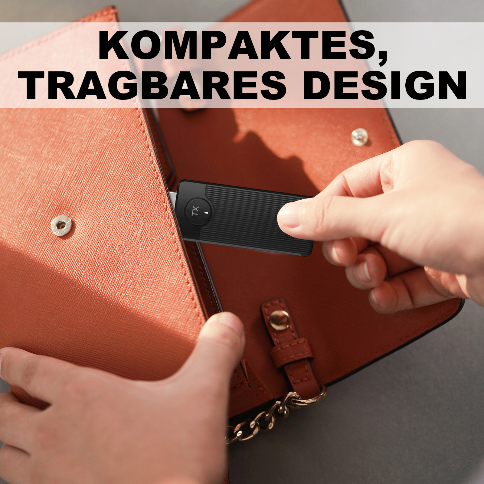 Eine Hand legt ein schwarzes Gerät in eine braune Handtasche. Die Tasche ist offen und zeigt ihr Inneres. Text oben.