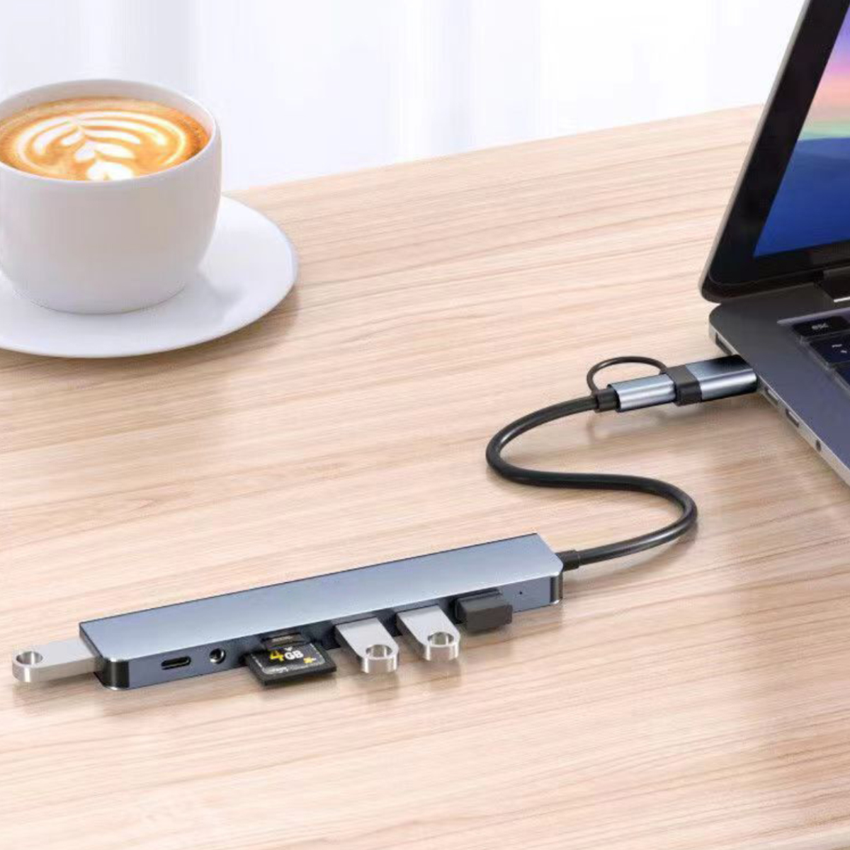 Ein Laptop mit angeschlossenem USB-Hub. Eine Tasse Kaffee steht in der Nähe des Laptops auf einer Holzoberfläche.