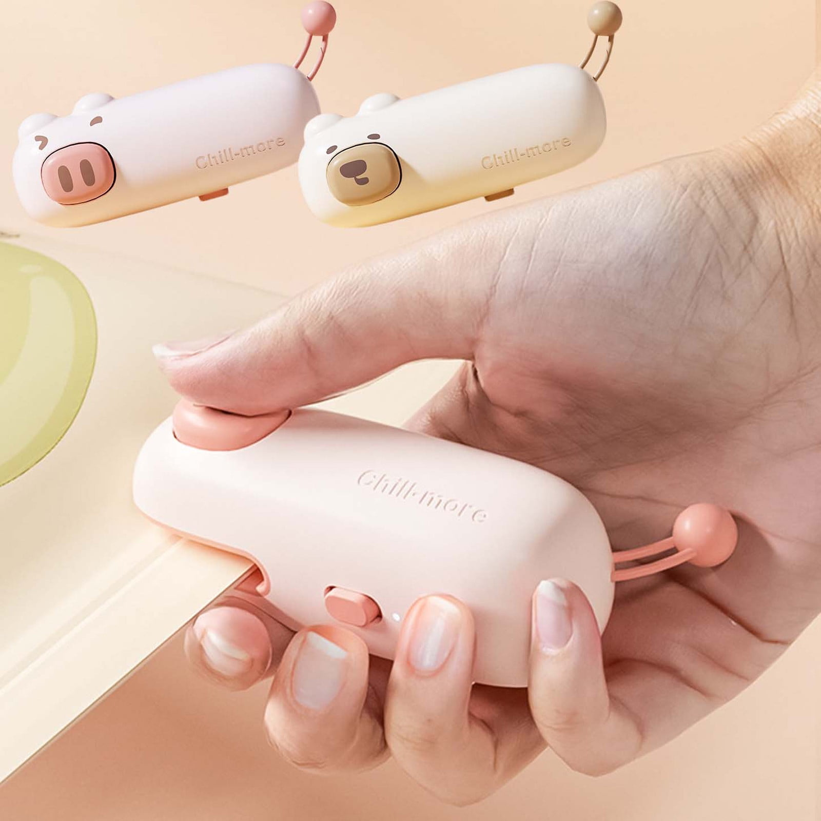 Eine Hand hält ein rosa 'Chill-more'-Gerät. Im Hintergrund befinden sich zwei ähnliche Geräte, eines in Schweineform, eines in Bärenform.