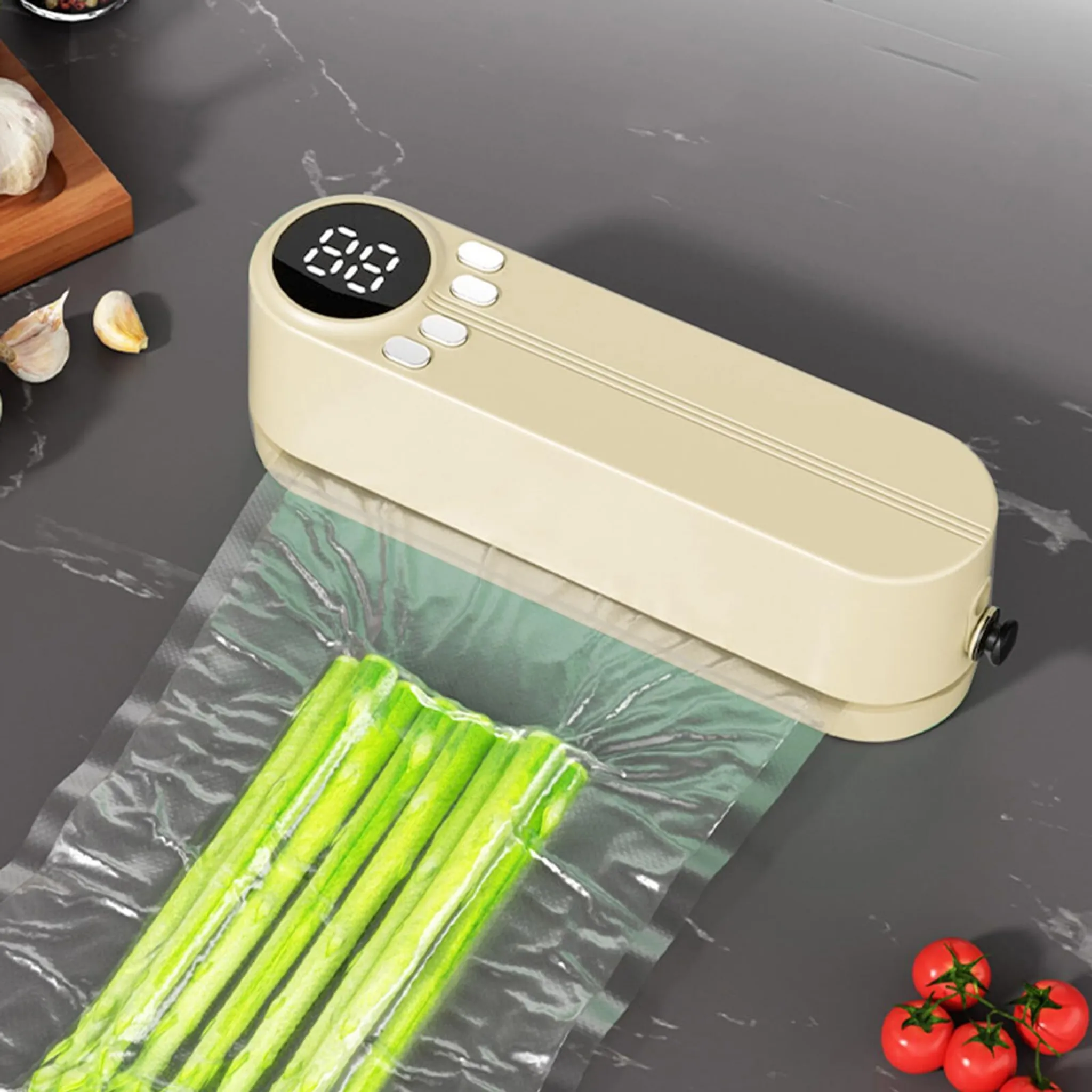 Ein beiges Vakuumiergerät versiegelt Spargel in einem Beutel. Knoblauch und Tomaten sind ebenfalls auf grauer Oberfläche vorhanden.