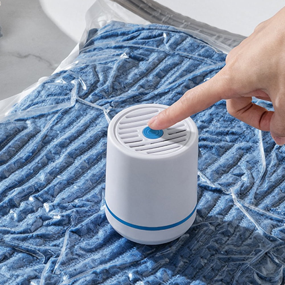 Eine Hand drückt einen blauen Knopf auf einem weißen Staubsauger. Er liegt auf einem blauen Textil in einer durchsichtigen Plastiktüte. Der Staubsauger hat einen blauen Sockel.