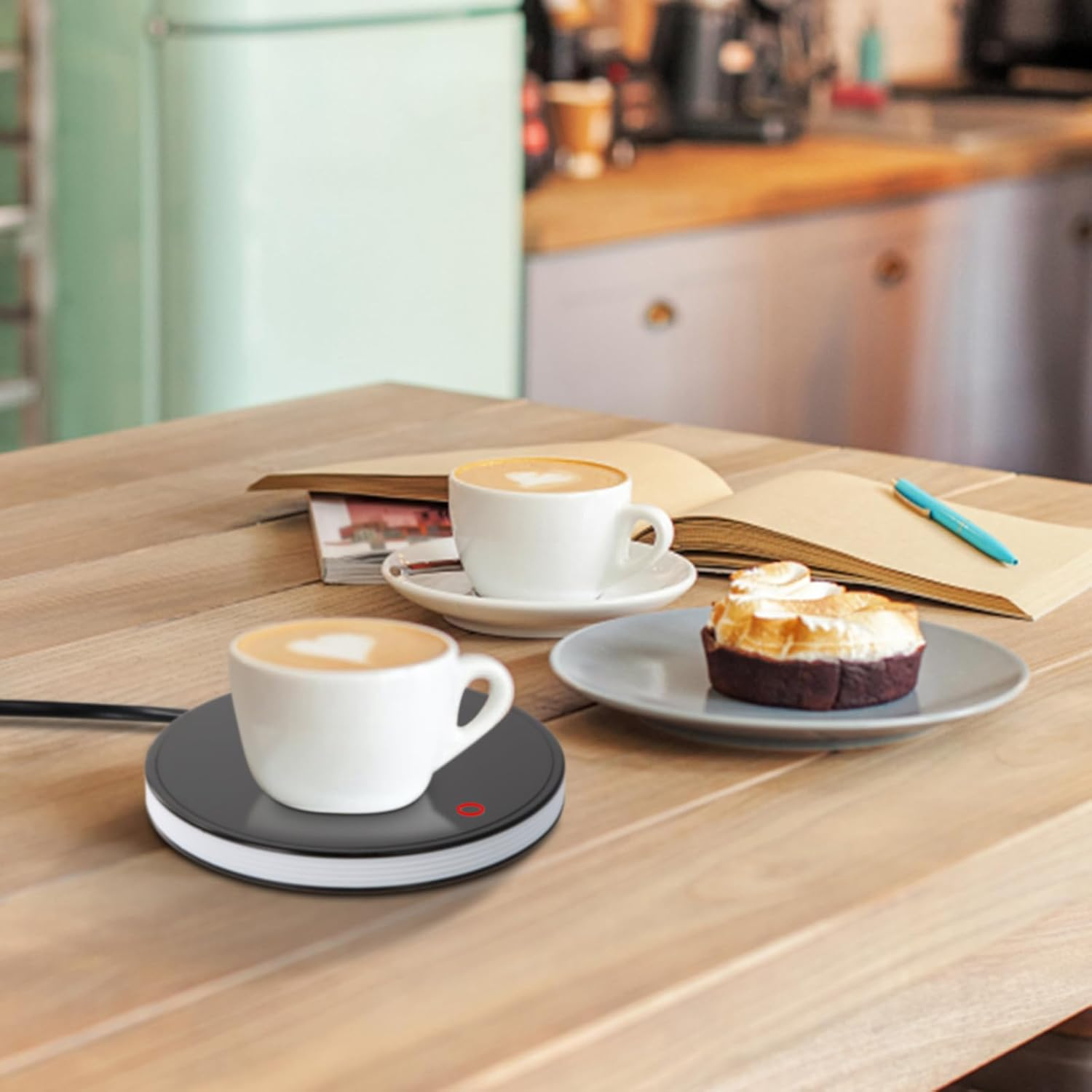 Ein Tisch mit Kaffeetassen, einem Dessert und einem Notizbuch. Eine Tasse steht auf einem Wärmer. Hintergrund: Café.