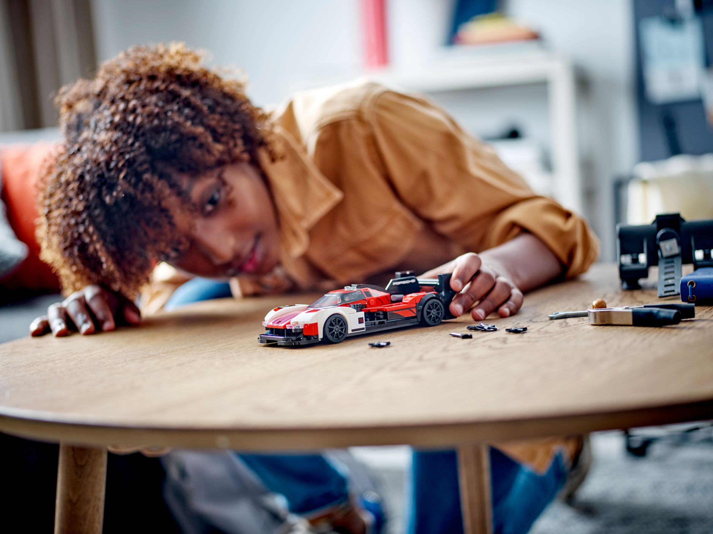 Eine Person beugt sich über einen Tisch und baut ein rot-weißes Spielzeugauto. Andere Gegenstände sind auf dem Tisch.