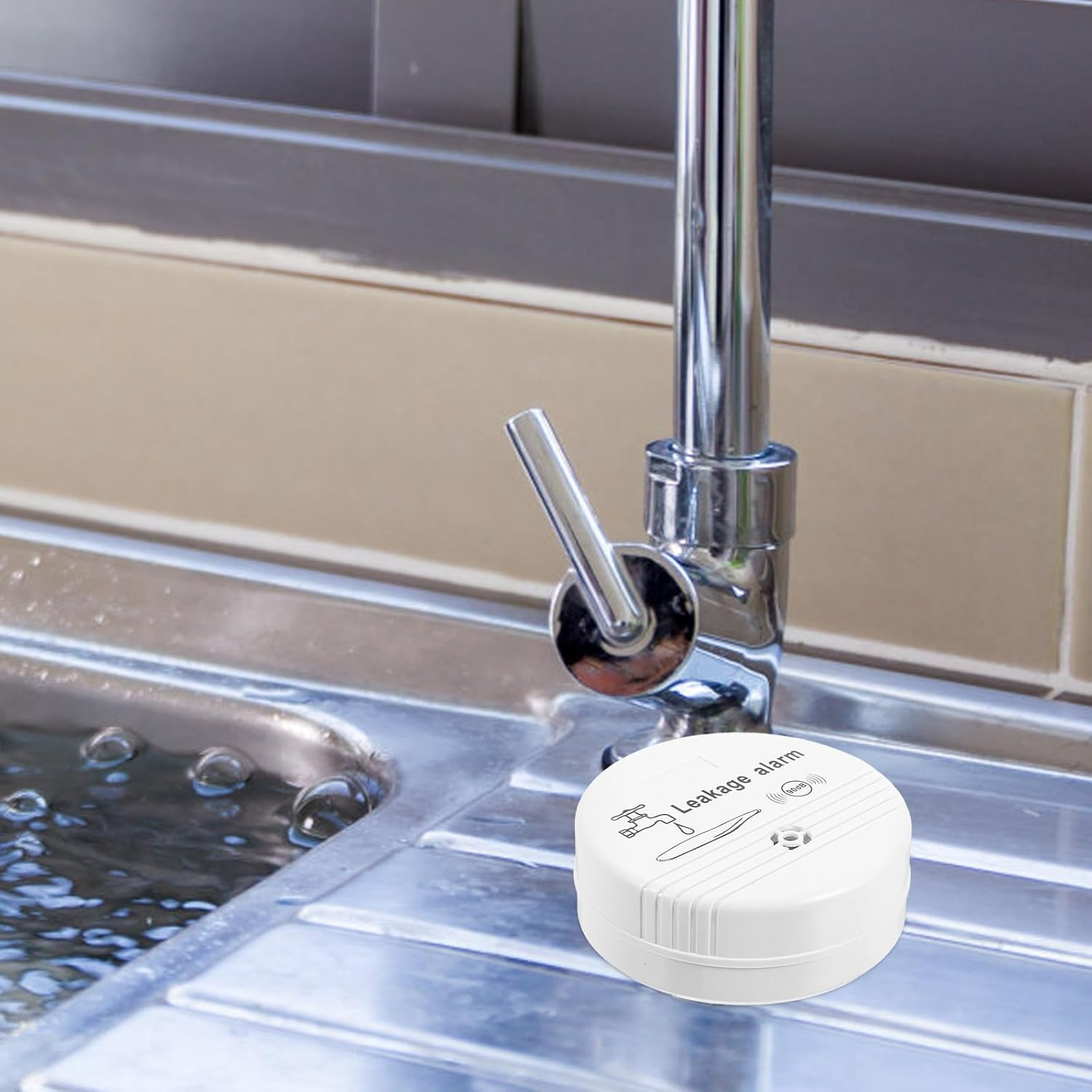 Ein weißer Leckagealarm liegt in einem Waschbecken mit Wasser. Über dem Waschbecken befindet sich ein Wasserhahn aus Chrom.