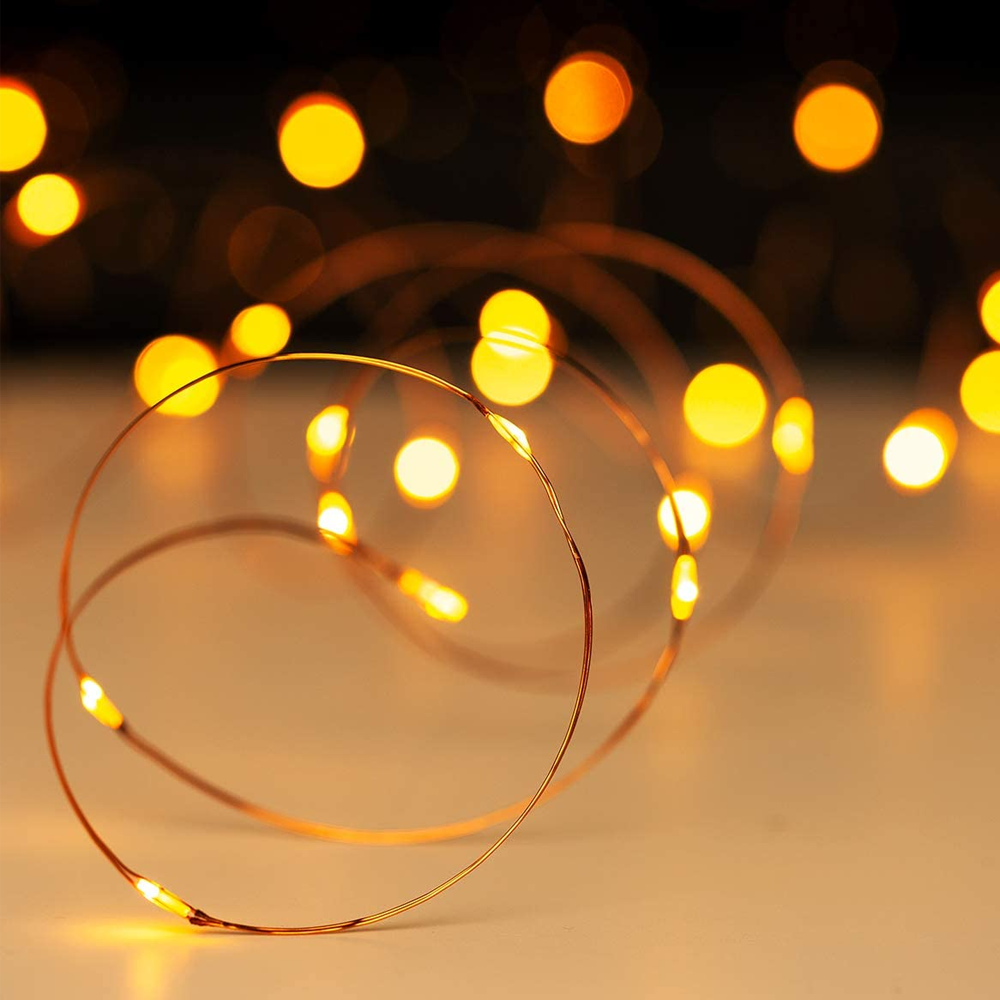 Nahaufnahme von Lichterketten. Kupferdraht mit kleinen, warmgelben Lichtern. Verschwommene Bokeh-Lichter im Hintergrund. Die Oberfläche ist hell.